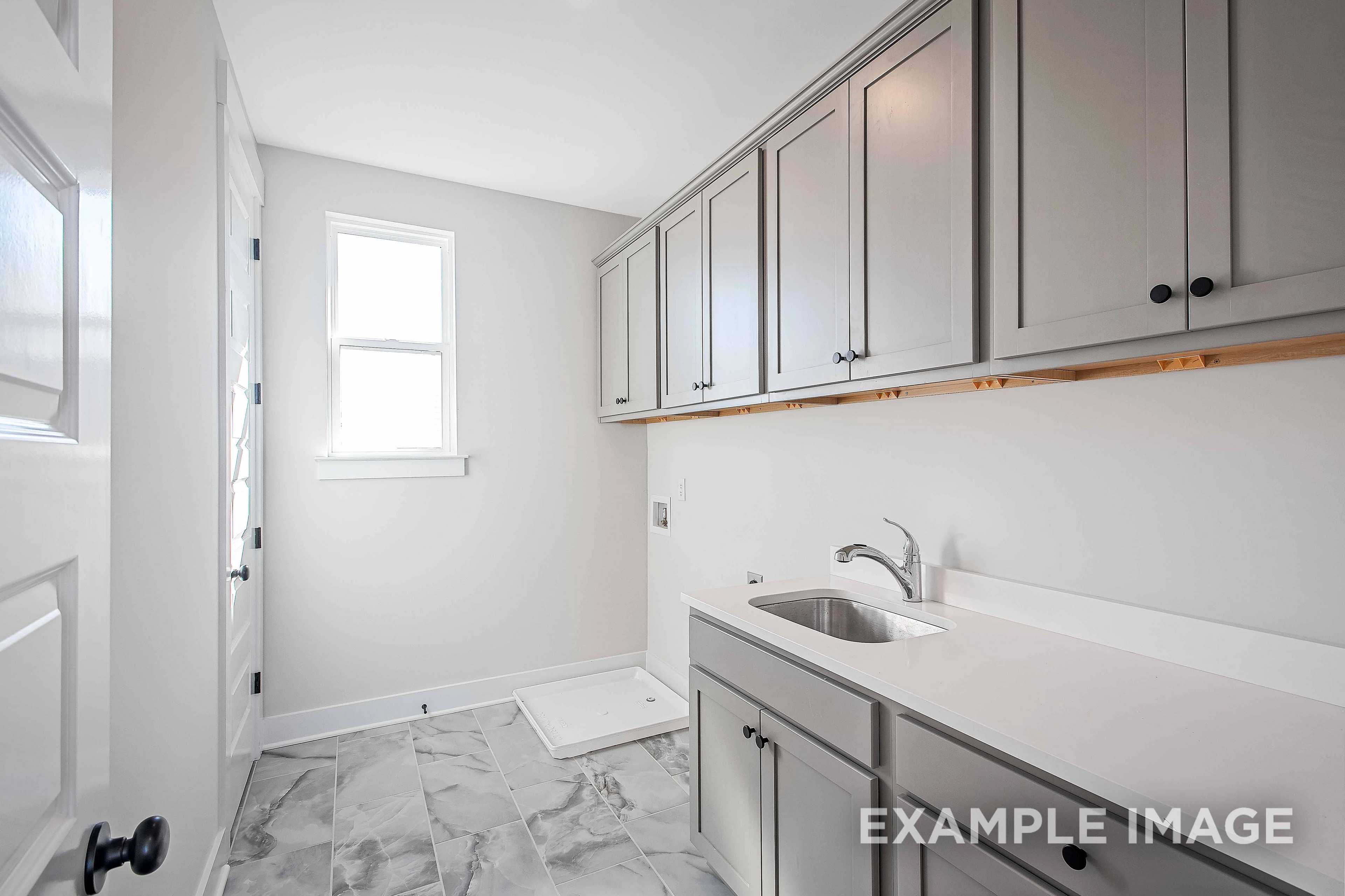 Modern laundry room in The Alston A showcasing gray shaker cabinets, utility sink, and tiled flooring