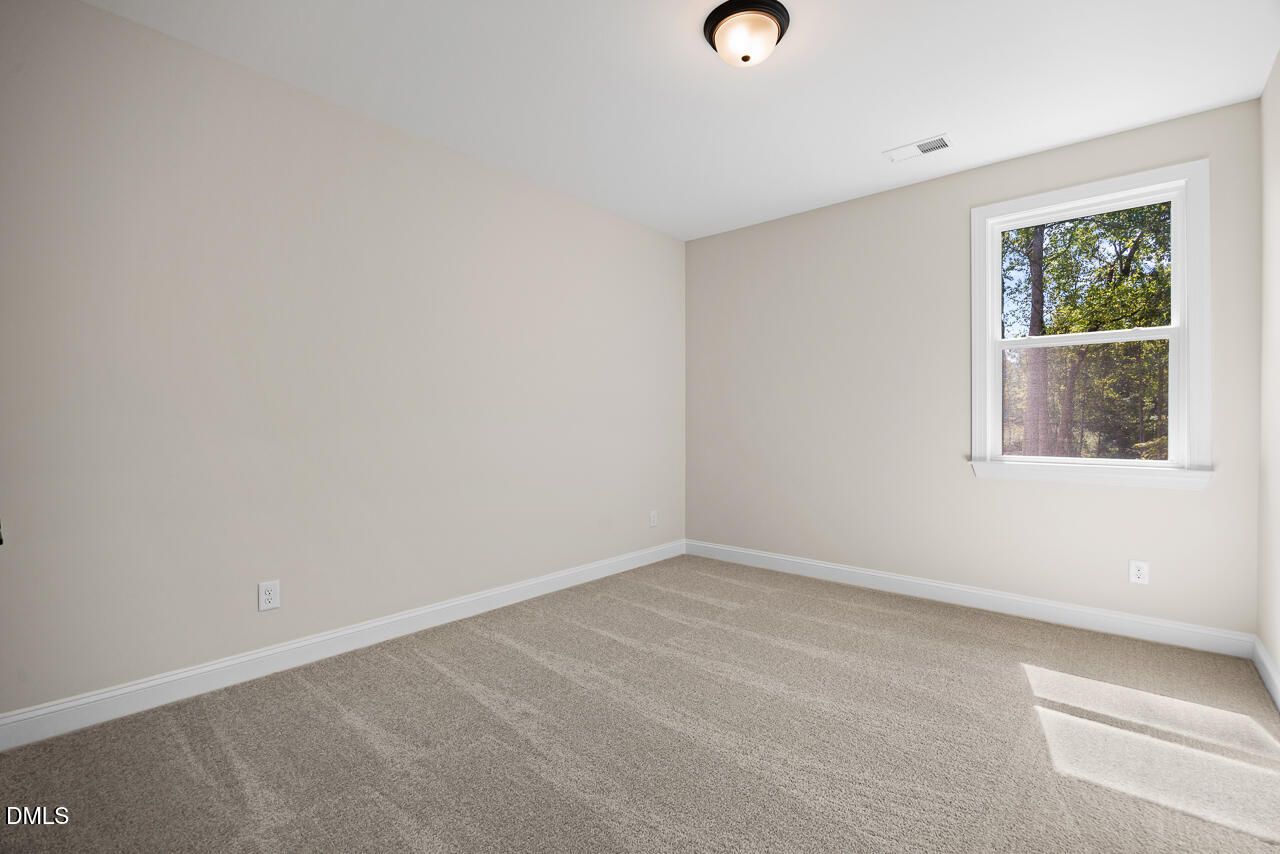 Bright empty bedroom with neutral walls, carpet flooring, and window overlooking trees in Davidson Homes Crawford D plan, Wake Forest NC