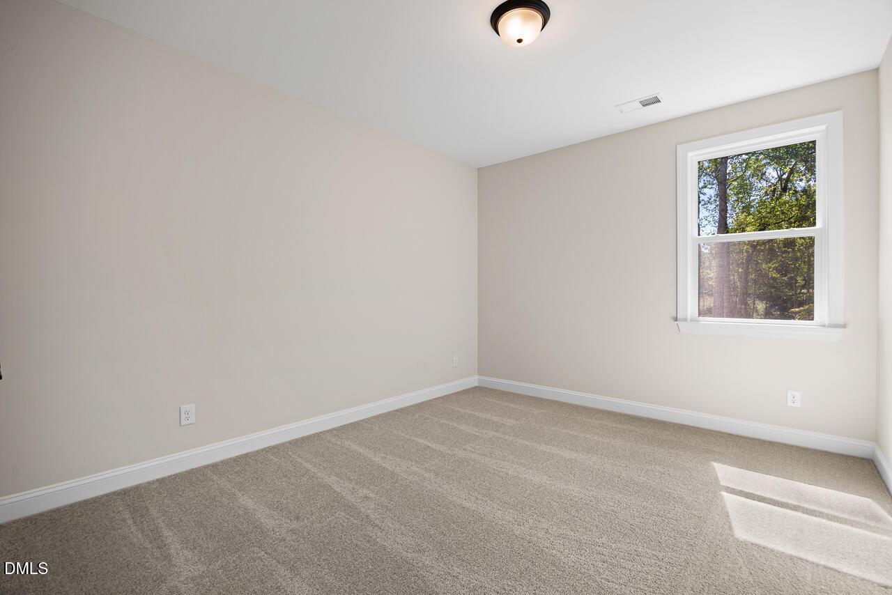 Bright empty bedroom with neutral walls, carpet flooring, and window overlooking trees in Davidson Homes Crawford D plan, Wake Forest NC