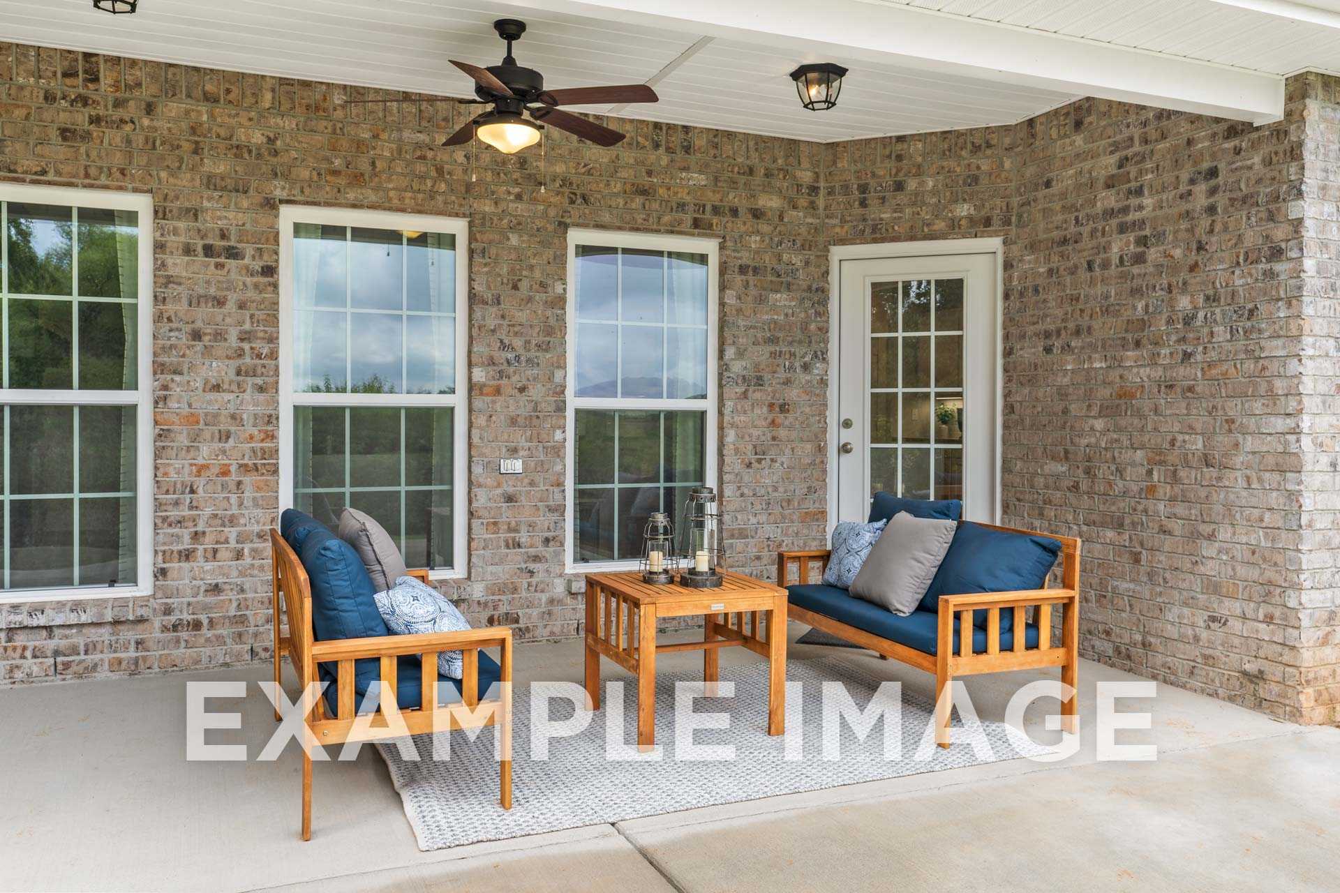 Spacious covered patio of The Harrison B with brick walls, large windows, ceiling fan, and cozy wooden seating