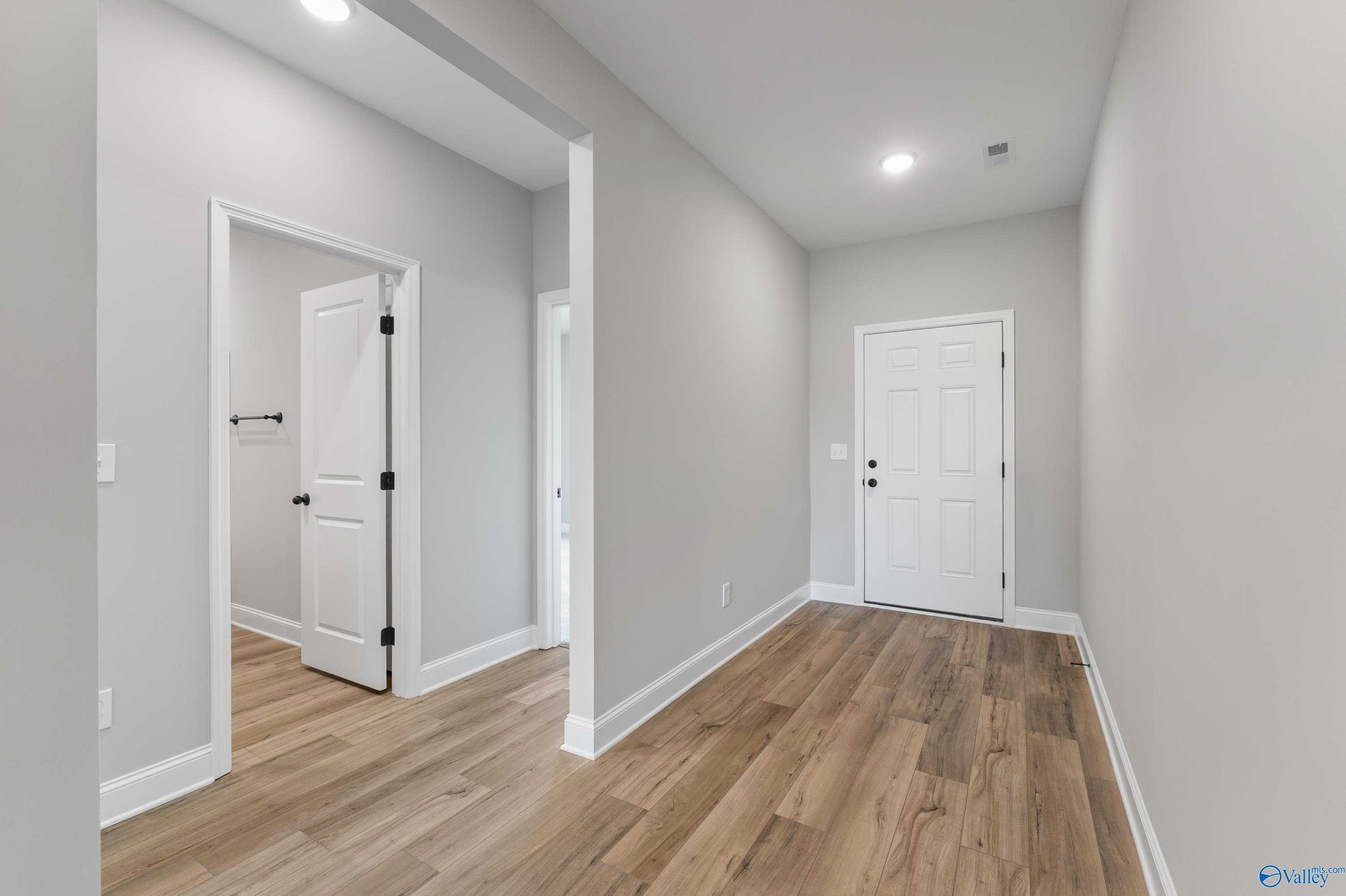 Bright hallway with light oak floors, gray walls, and white doors to bedroom and bath in Davidson Homes The Daphne C, Hazel Green, AL