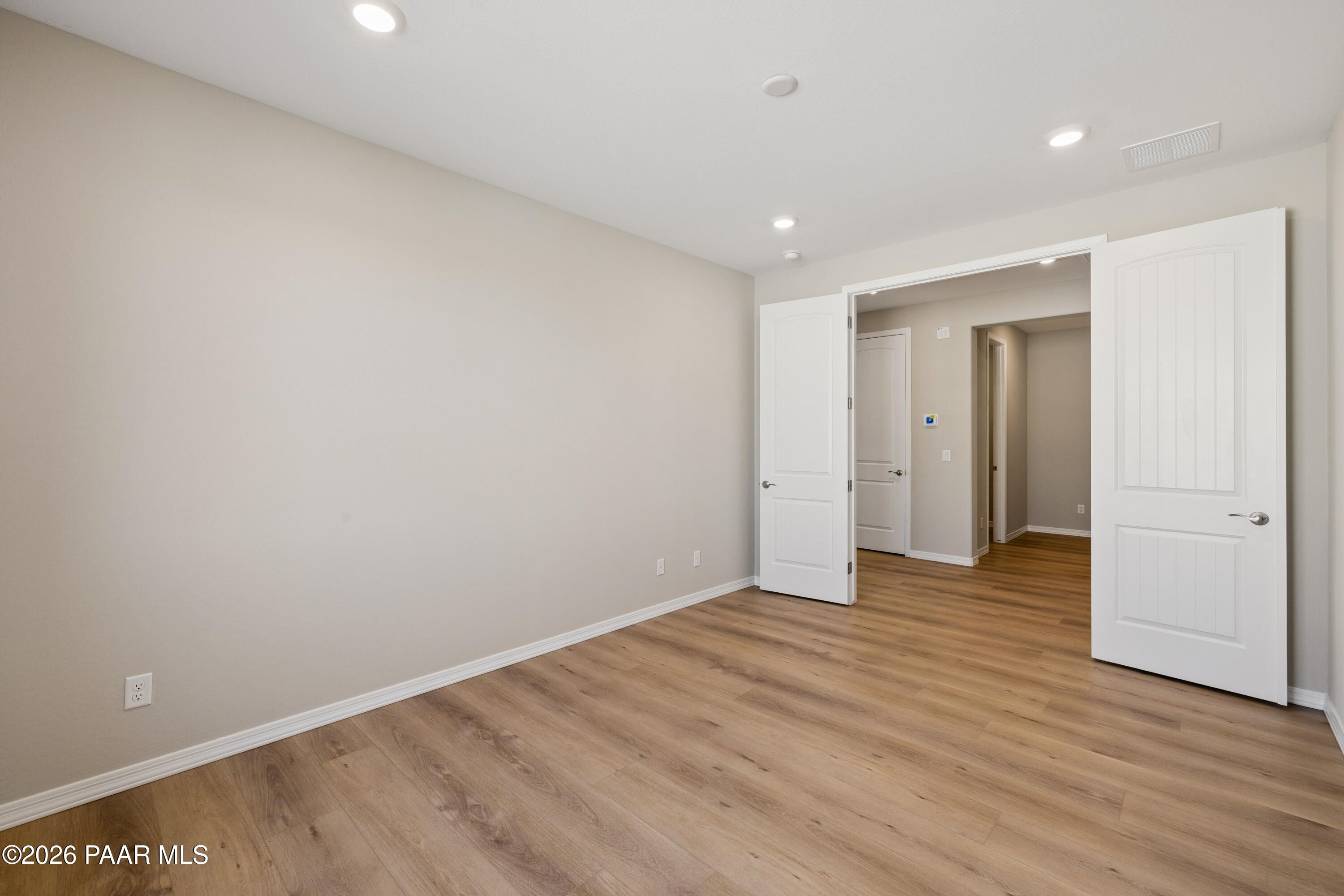 Spacious bedroom with open double doors, beige walls, and oak hardwood floors in Davidson Homes The Harmony A, Prescott Valley