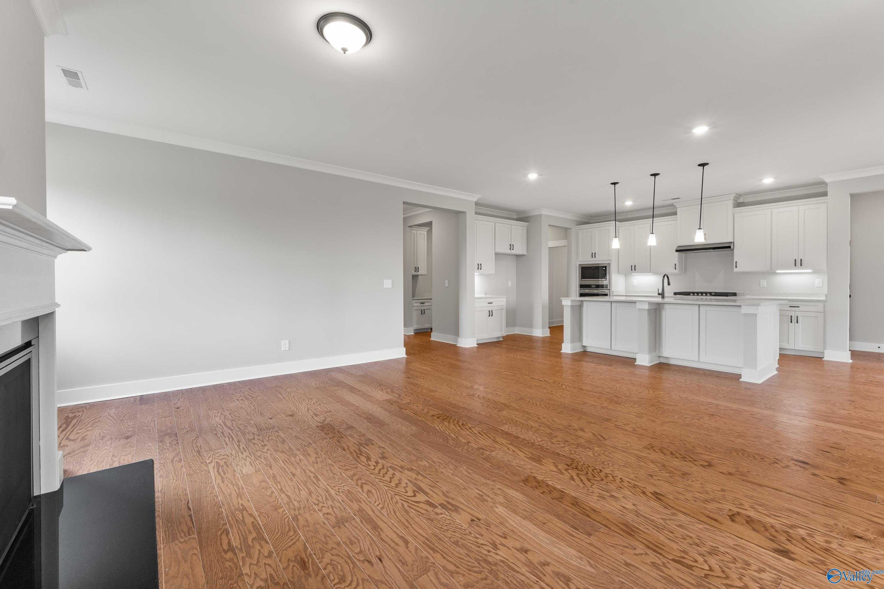 Open-concept great room with oak hardwood floors, white fireplace mantel, and adjacent kitchen island in Davidson Homes The Arcadia, Huntsville