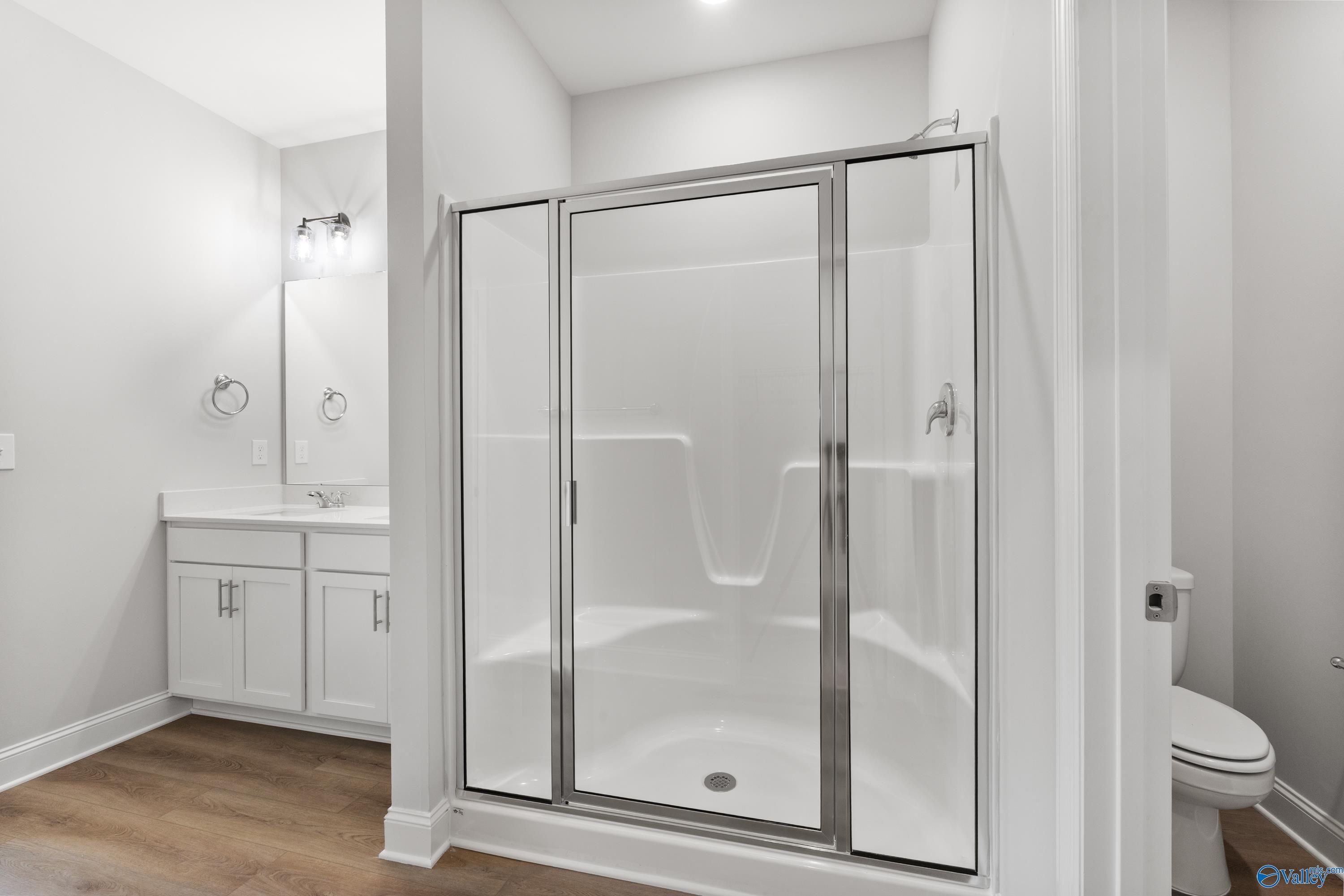 Elegant white bathroom with glass shower enclosure, single vanity, and wood flooring in Davidson Homes The Daphne, Hazel Green, Alabama