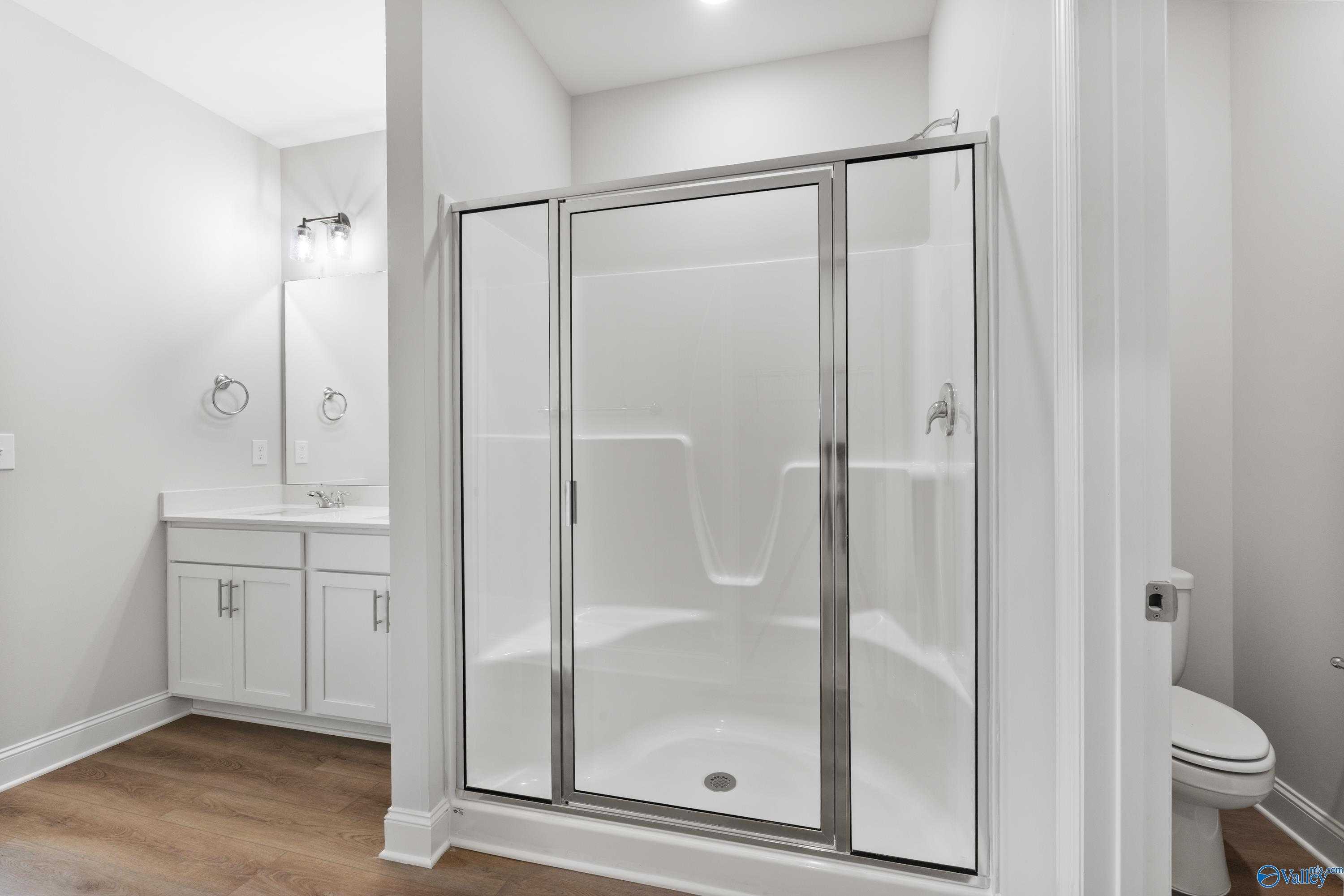 Elegant white bathroom with glass shower enclosure, single vanity, and wood flooring in Davidson Homes The Daphne, Hazel Green, Alabama
