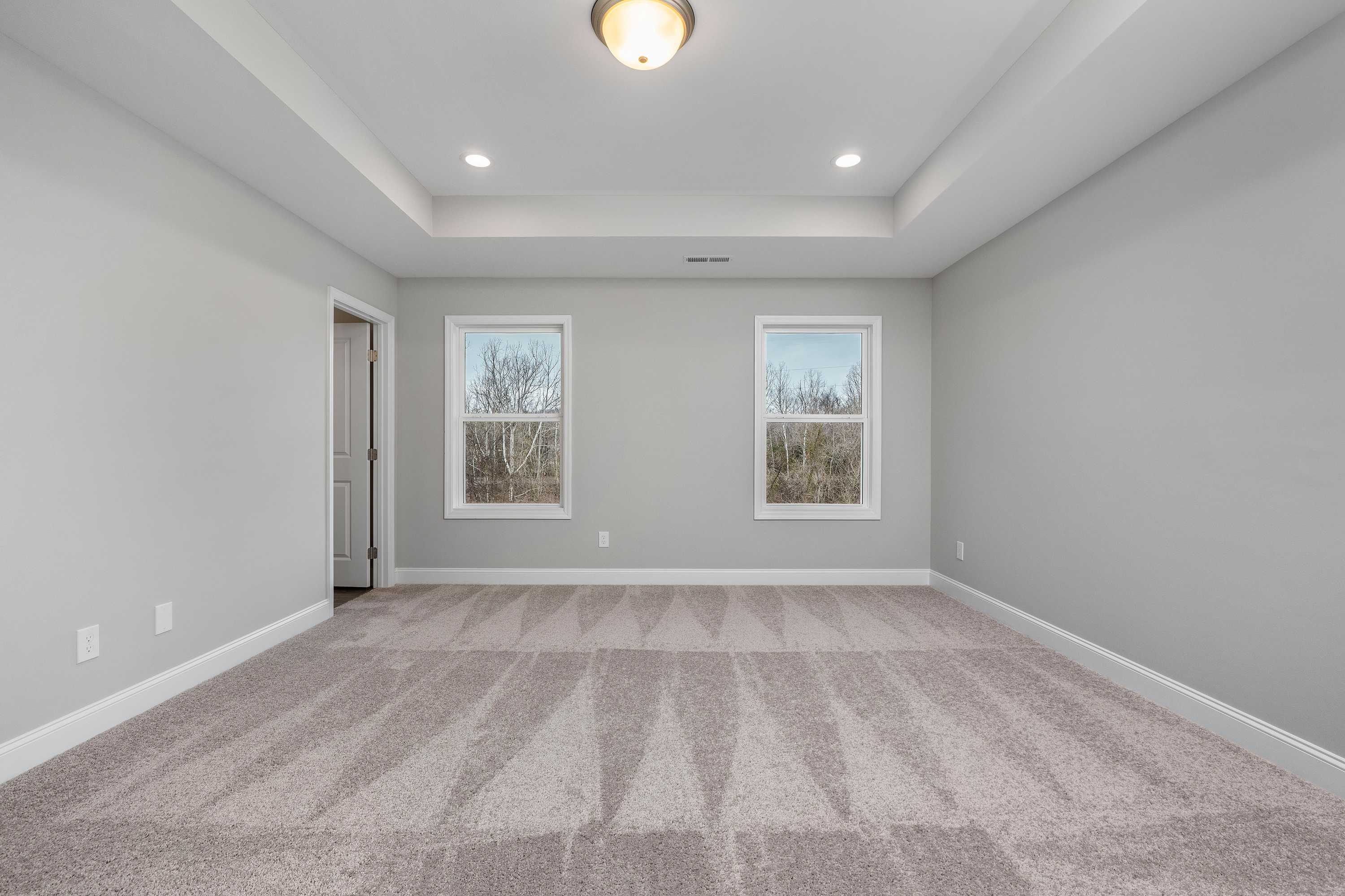 Spacious master bedroom in The Aiken by Davidson Homes featuring gray walls, carpeted floors, and large windows