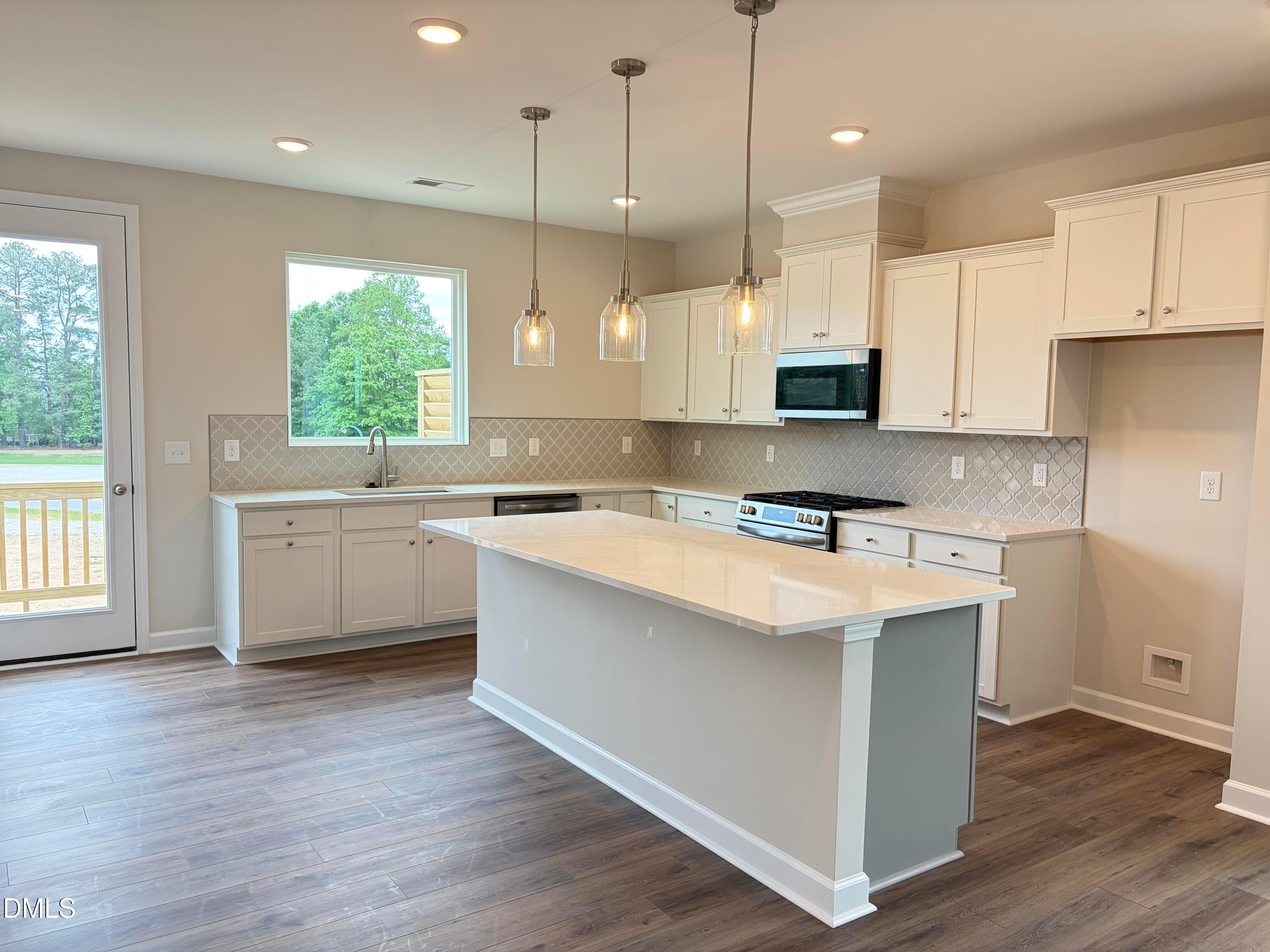Modern white shaker kitchen with quartz island, stainless appliances, subway tile backsplash, and backyard view in Davidson Homes Avery, Knightdale NC