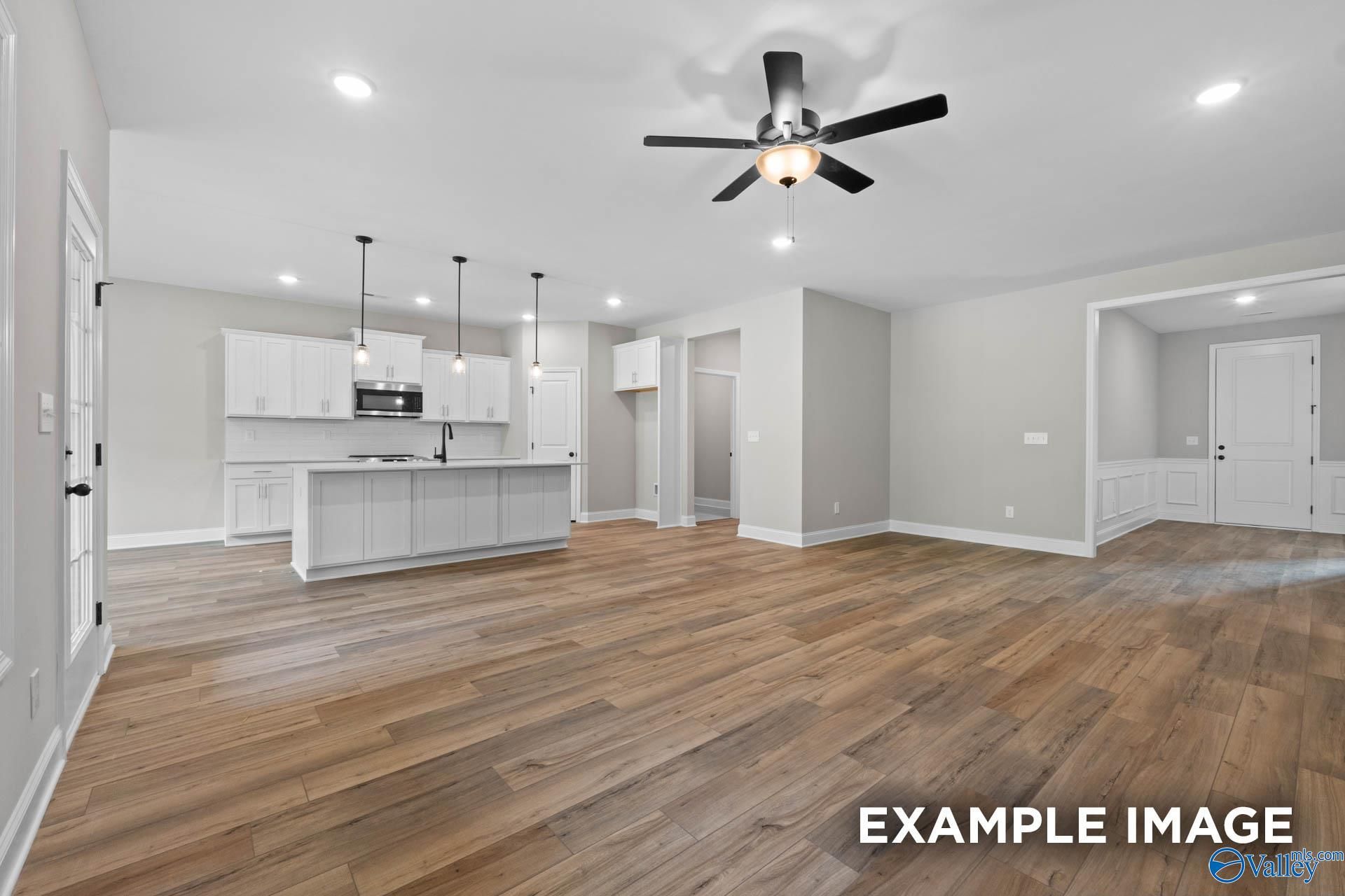 Open-concept kitchen with white cabinets, island, stainless appliances, and adjacent living area on hardwood floors in Davidson Homes Montgomery B, Toney, AL