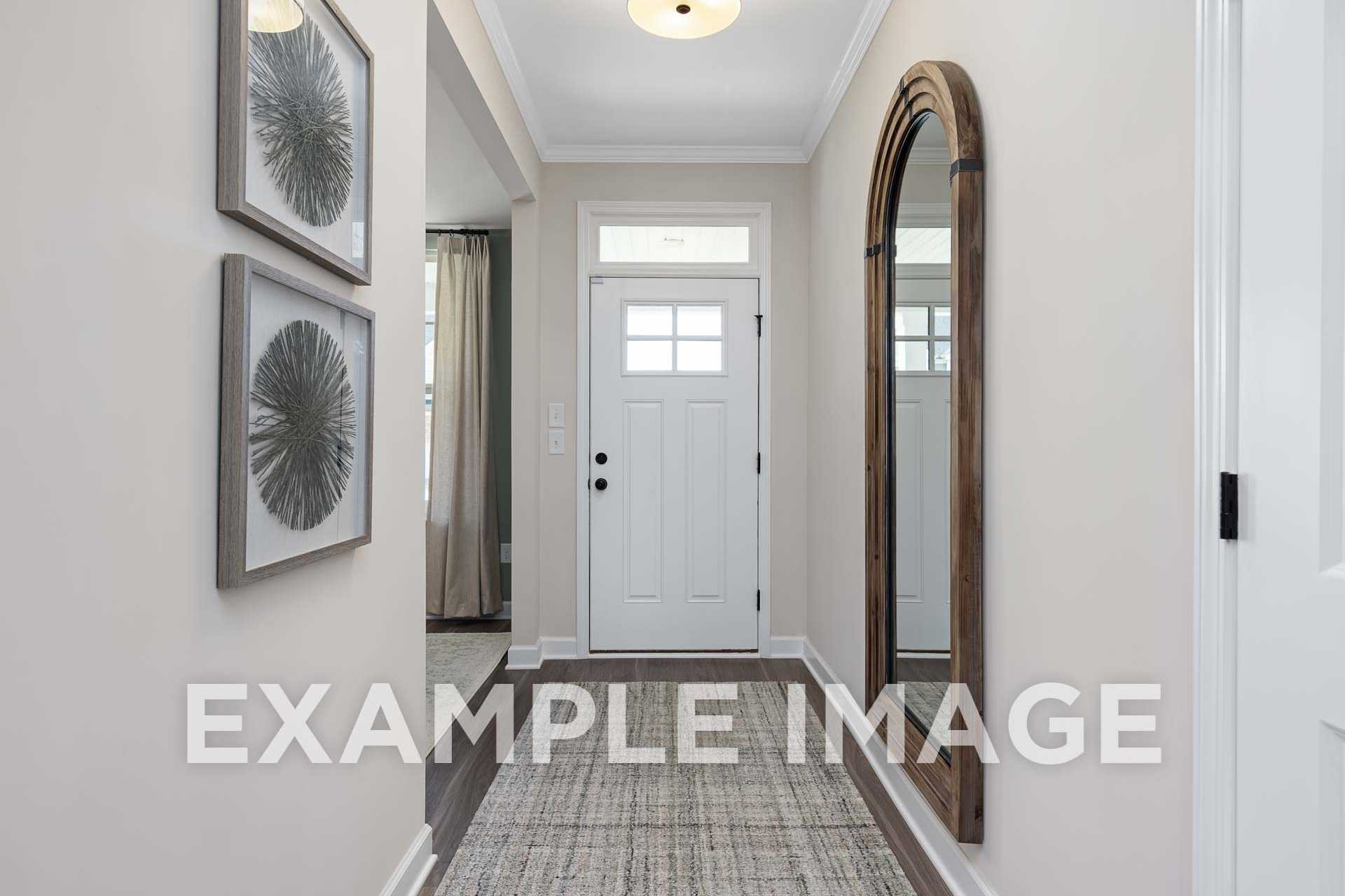 Spacious entry hallway in The Willow F home design featuring arched wooden mirror, framed art, white door, and neutral walls