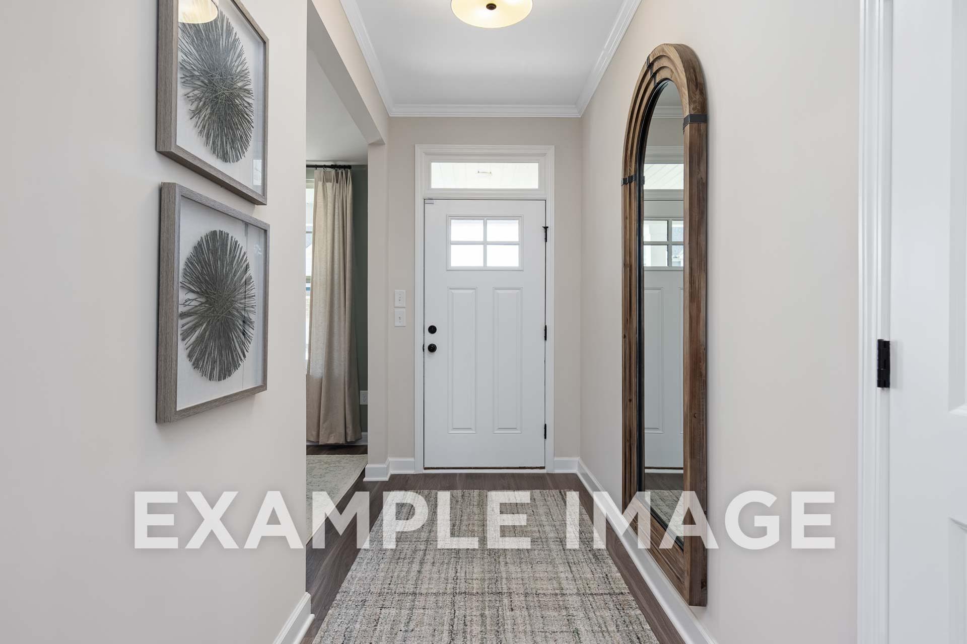 Bright hallway in The Willow E home with arched wooden mirror, framed circular art, white door, and soft lighting