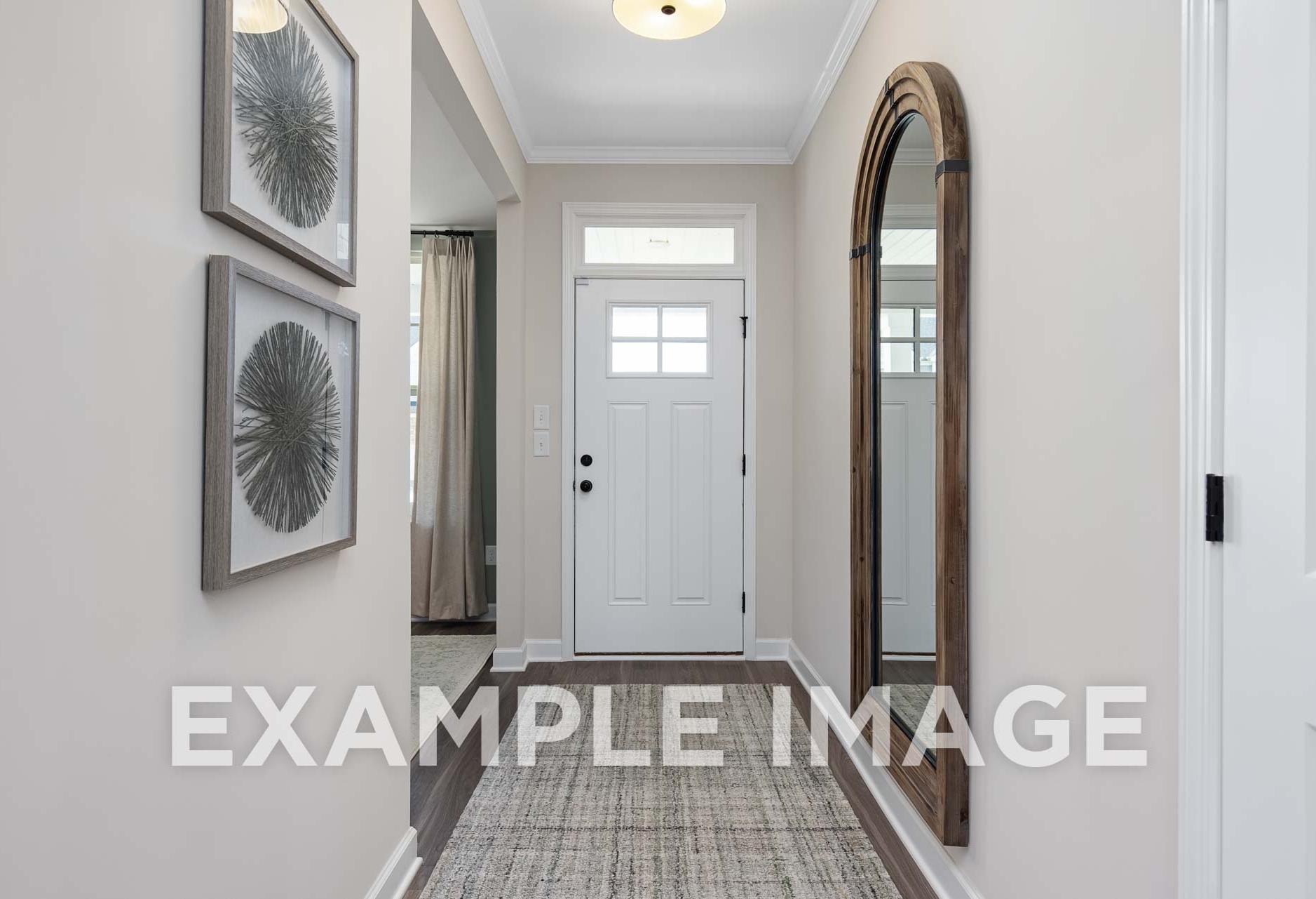 Bright hallway in The Willow E home with arched wooden mirror, framed circular art, white door, and soft lighting