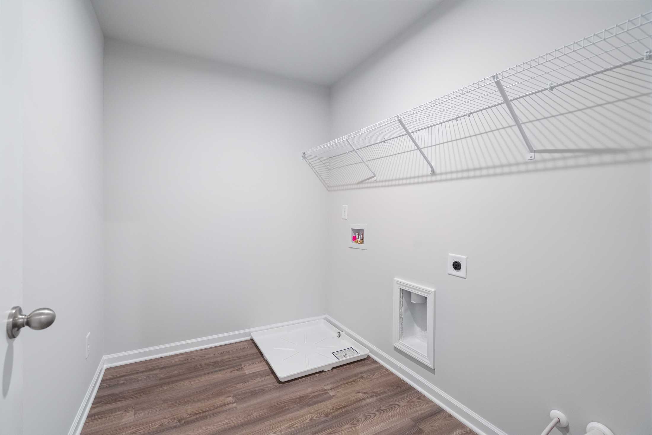 Spacious laundry room in The Cary A by Davidson Homes featuring wire shelving, washer dryer hookups, and hardwood floors in Winder GA