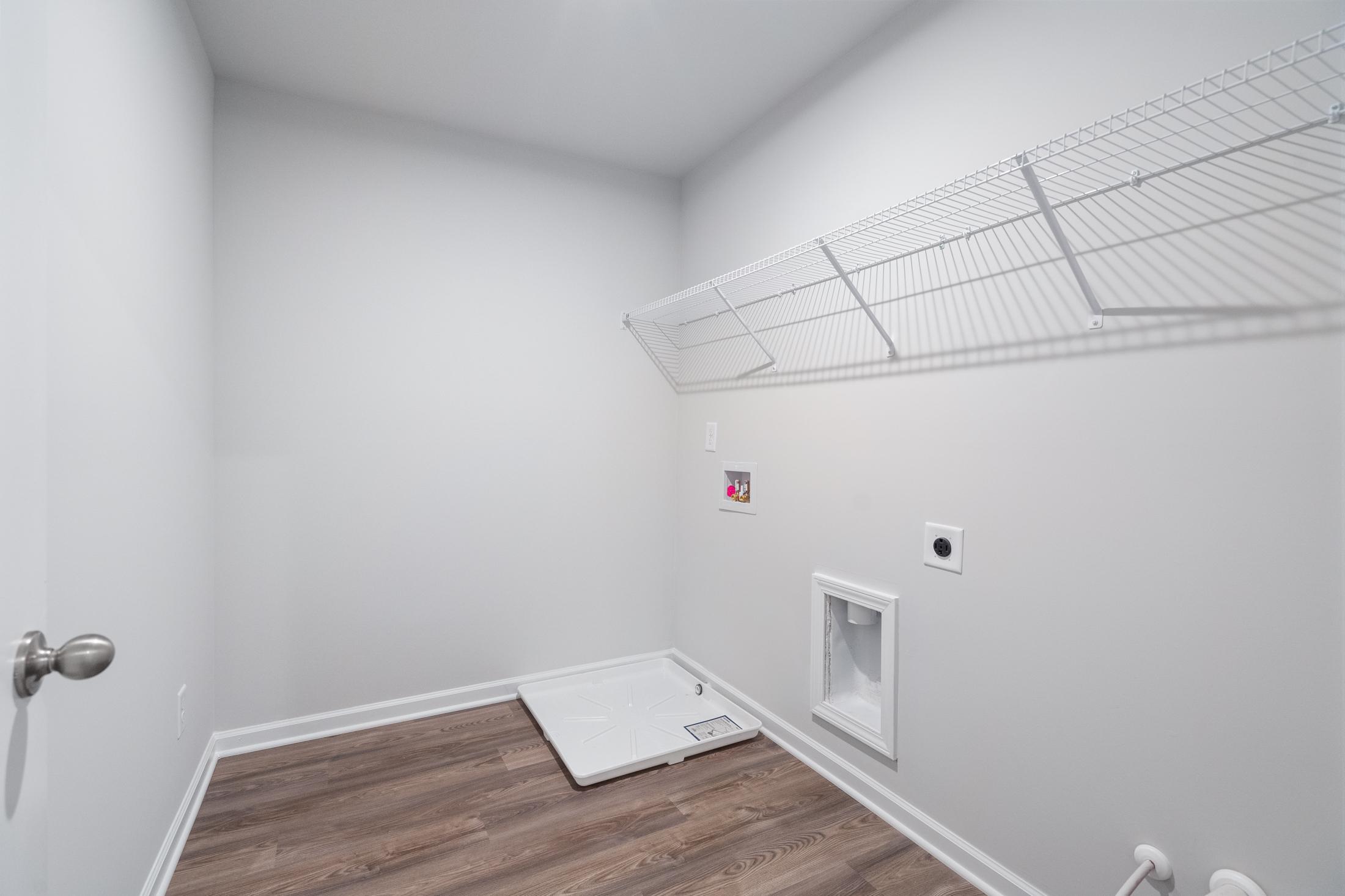 Spacious laundry room in The Cary A by Davidson Homes featuring wire shelving, washer dryer hookups, and hardwood floors in Winder GA