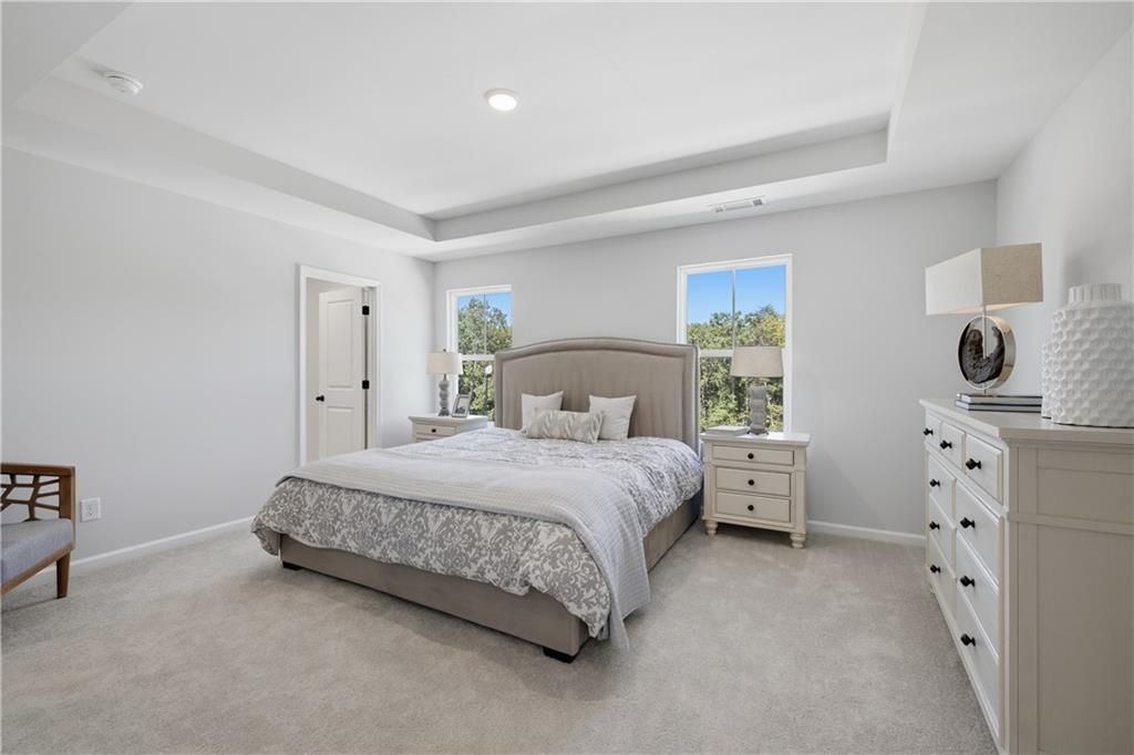 Bright primary bedroom with tray ceiling, upholstered headboard, and carpet in Davidson Homes Hartwell C plan, The Bluffs, Canton GA