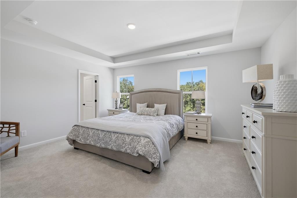 Bright primary bedroom with tray ceiling, upholstered headboard, and carpet in Davidson Homes Hartwell C plan, The Bluffs, Canton GA