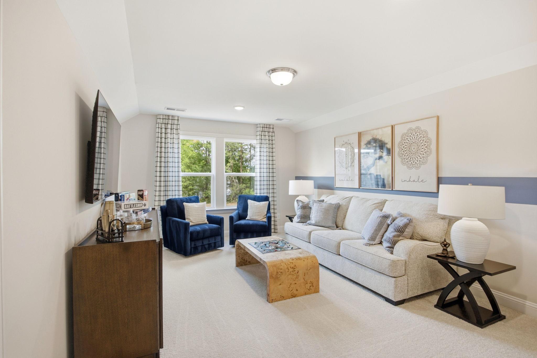 Cozy family room at Enclave at Belmont in Belmont NC with beige sectional sofa, blue velvet chairs, burl wood coffee table, and wall art
