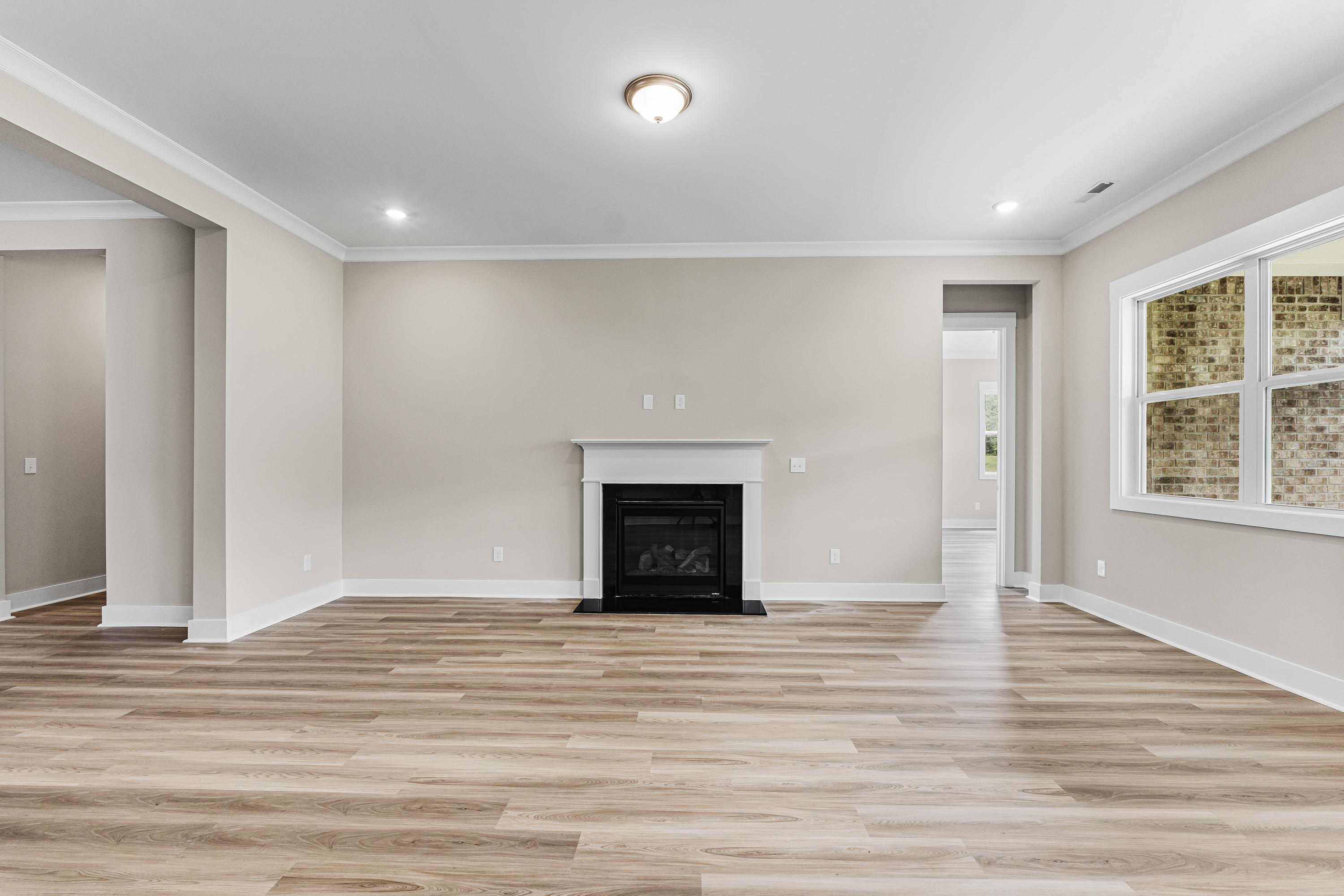 Spacious living room in The Oxford A with beige walls, hardwood floors, and modern gas fireplace by Evermore Homes