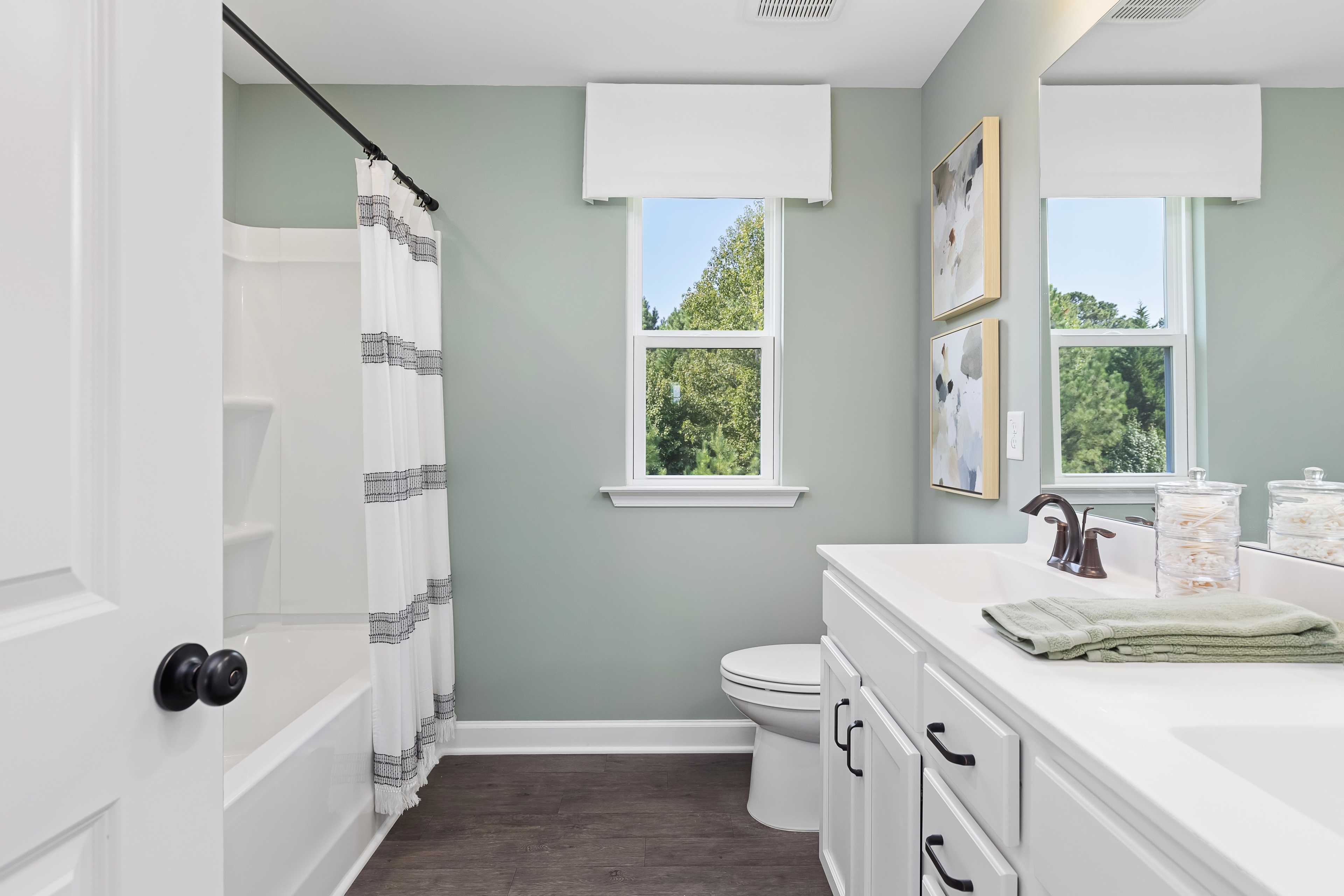 Spacious bathroom with sage green walls, white striped shower curtain, bathtub and vanity at Woodland Crossing in Zebulon NC