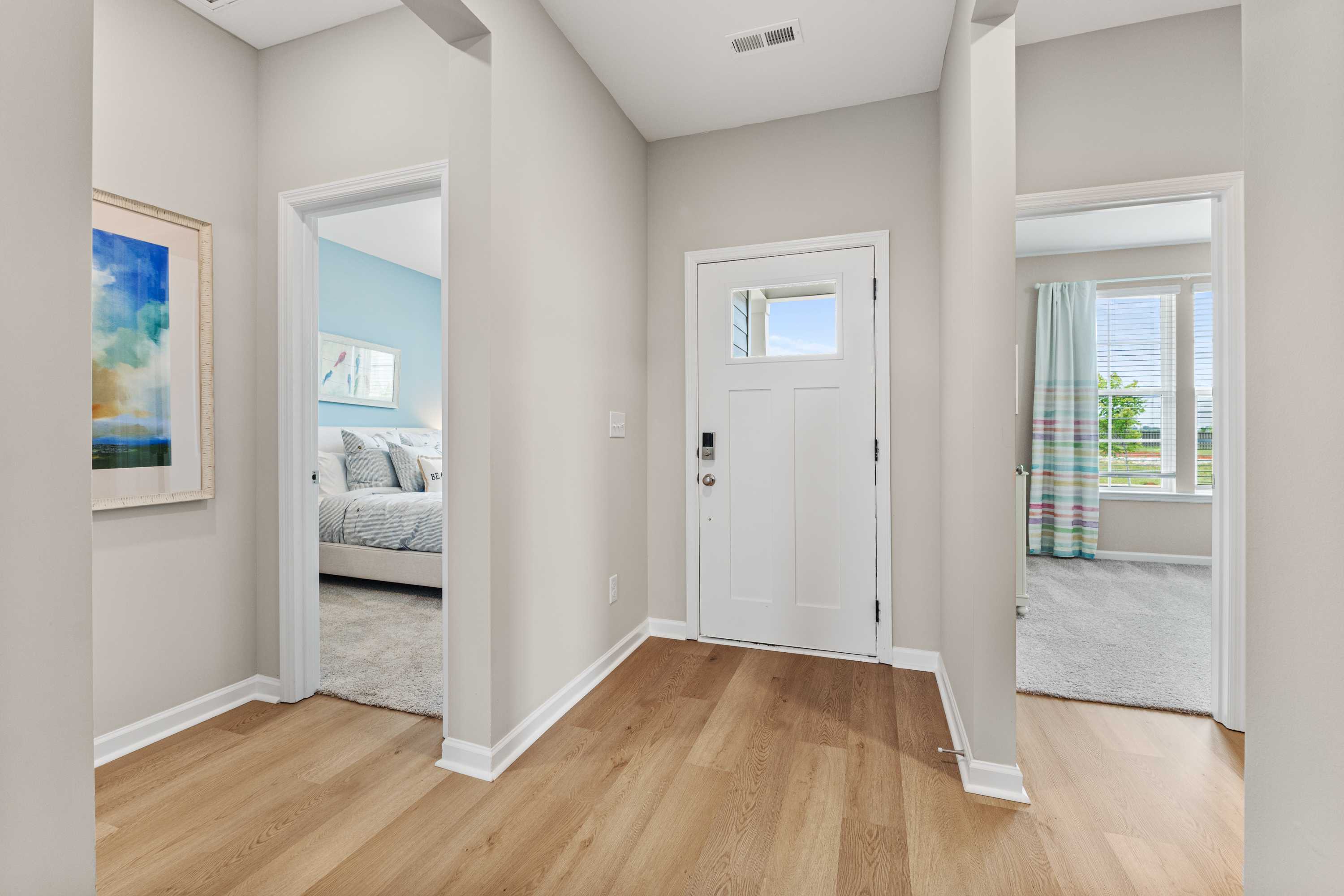 Bright entry hallway in Anderson Farm home, Athens Alabama with hardwood floors, white front door, and open bedroom view