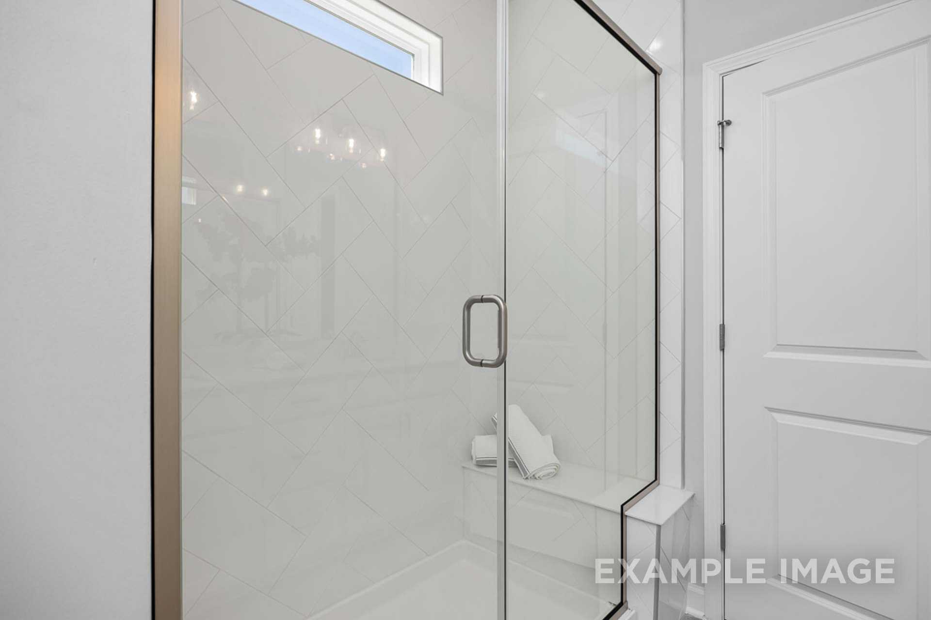 Modern frameless glass walk-in shower in The Carter B master bath with white subway tiles, built-in bench, and clerestory window