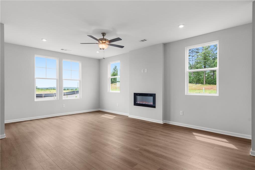 Spacious living room featuring electric fireplace, hardwood floors, and large windows overlooking trees in Davidson Homes Monroe B, Emerson, GA