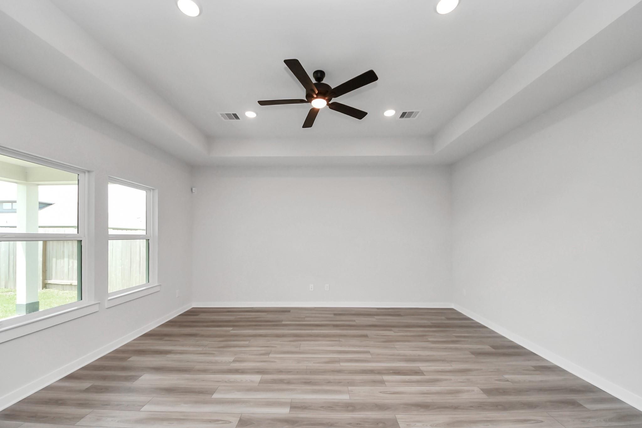 Spacious living room with tray ceiling and ceiling fan in The Everett C floor plan at River Ranch Meadows, Dayton, Texas.