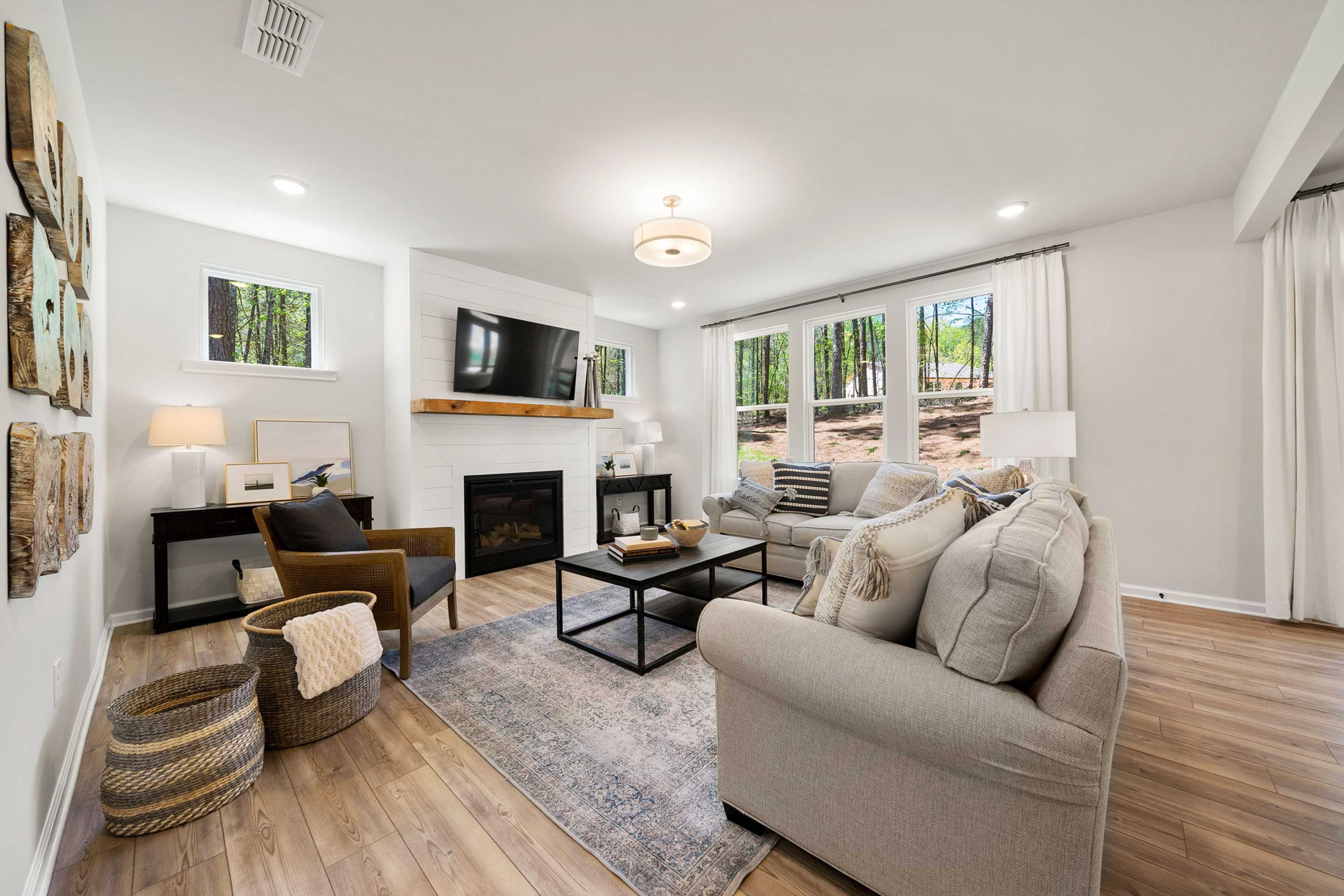 Cozy living room at Riverwood in Dallas Georgia by Davidson Homes featuring gas fireplace, gray sofa, hardwood floors, and wooded window views