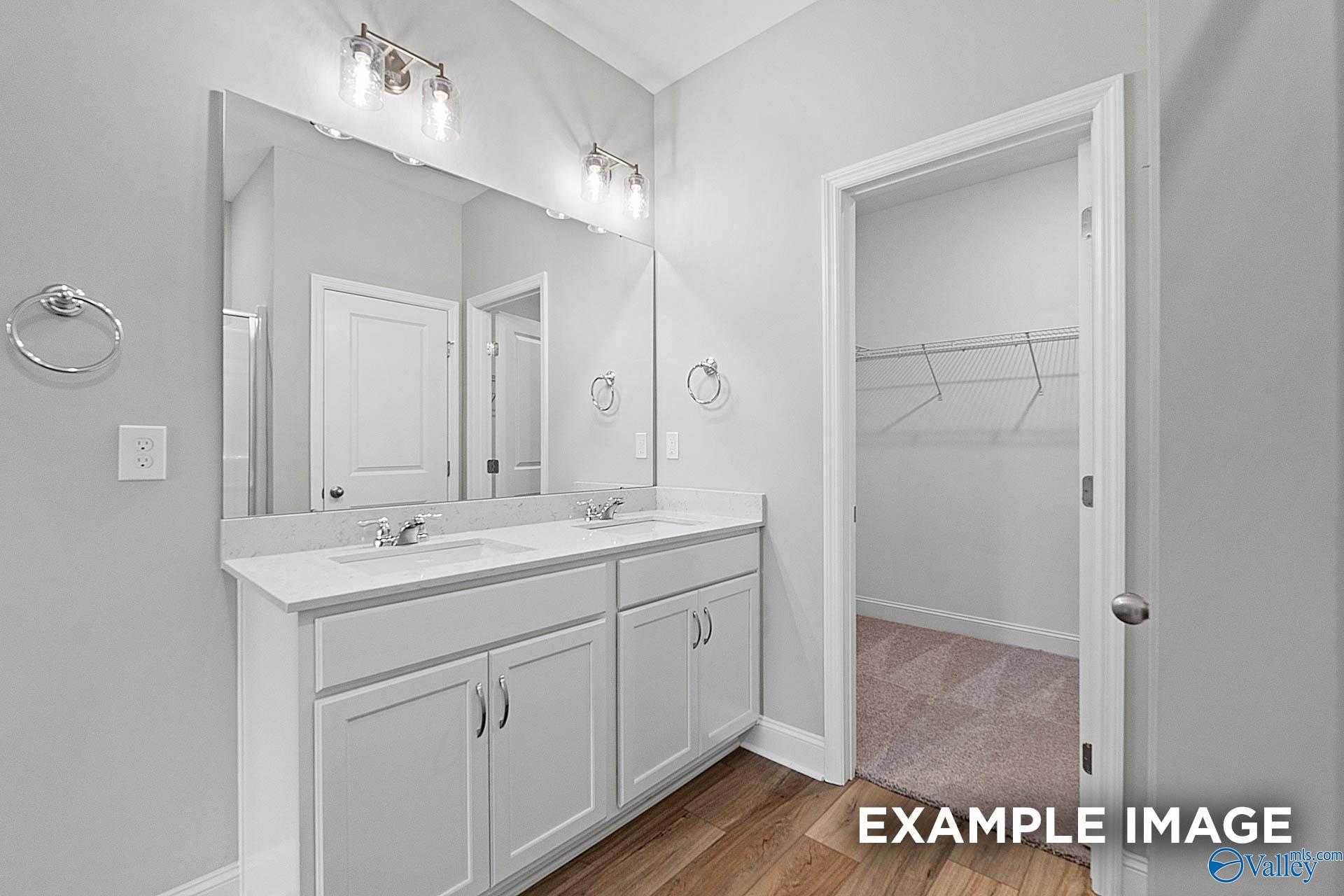 Modern master bathroom featuring double vanity sinks, large mirrors, and adjacent walk-in closet in Davidson Homes The Franklin E, Hazel Green, Alabama