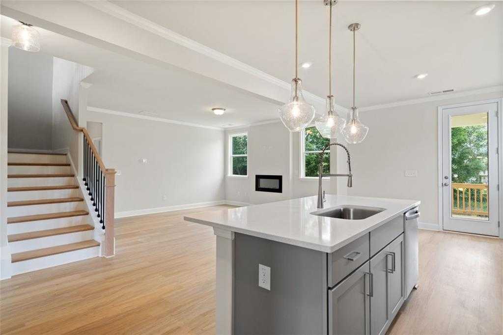 Open-concept kitchen with white quartz island, gray cabinets, pendant lights, and adjacent living space featuring gas fireplace in Davidson Homes The Willow D at Wehunt Meadows, Hoschton
