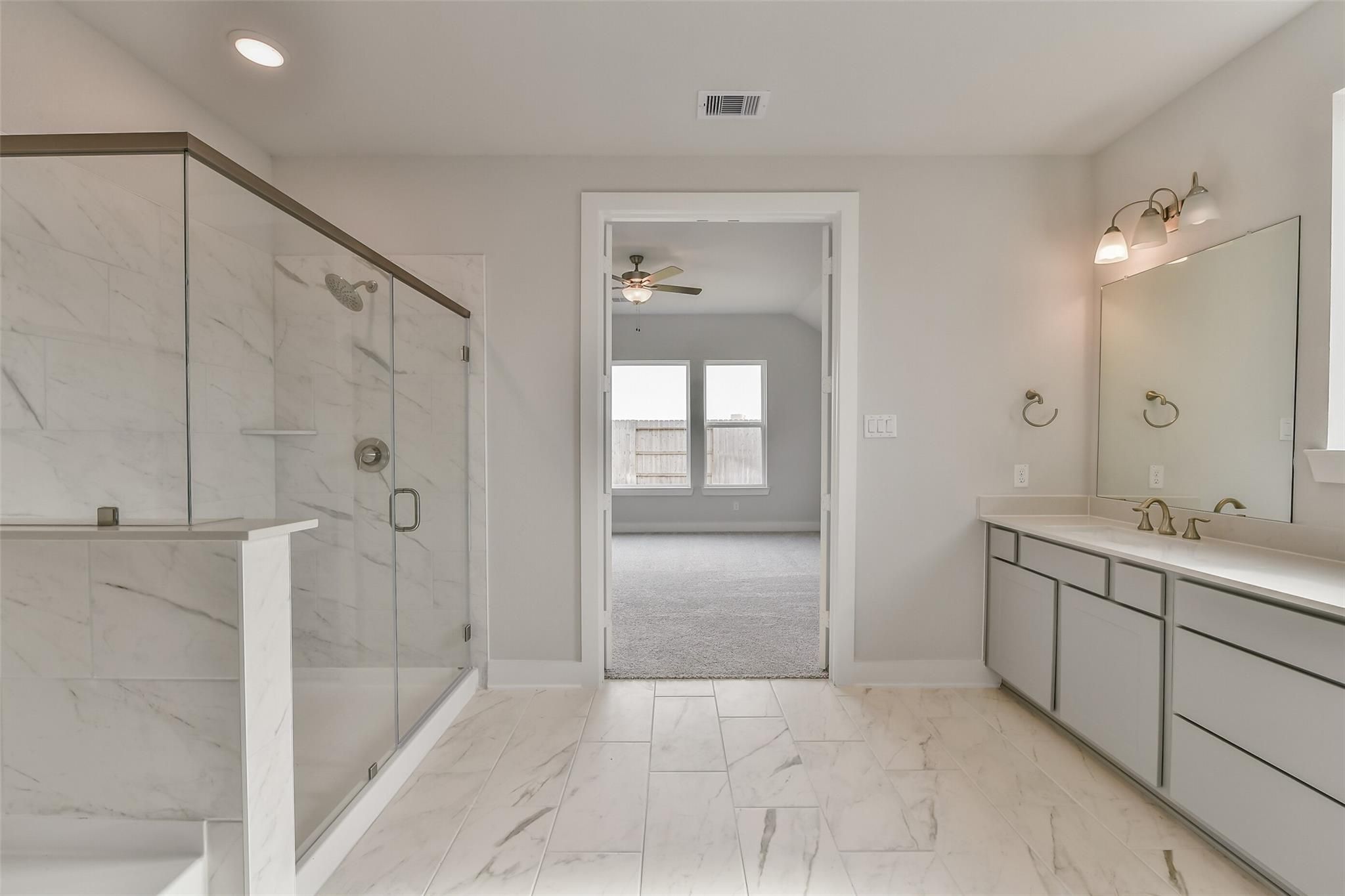 Modern master bathroom featuring frameless glass shower, double vanity with gold fixtures in Davidson Homes The George A, Lago Mar