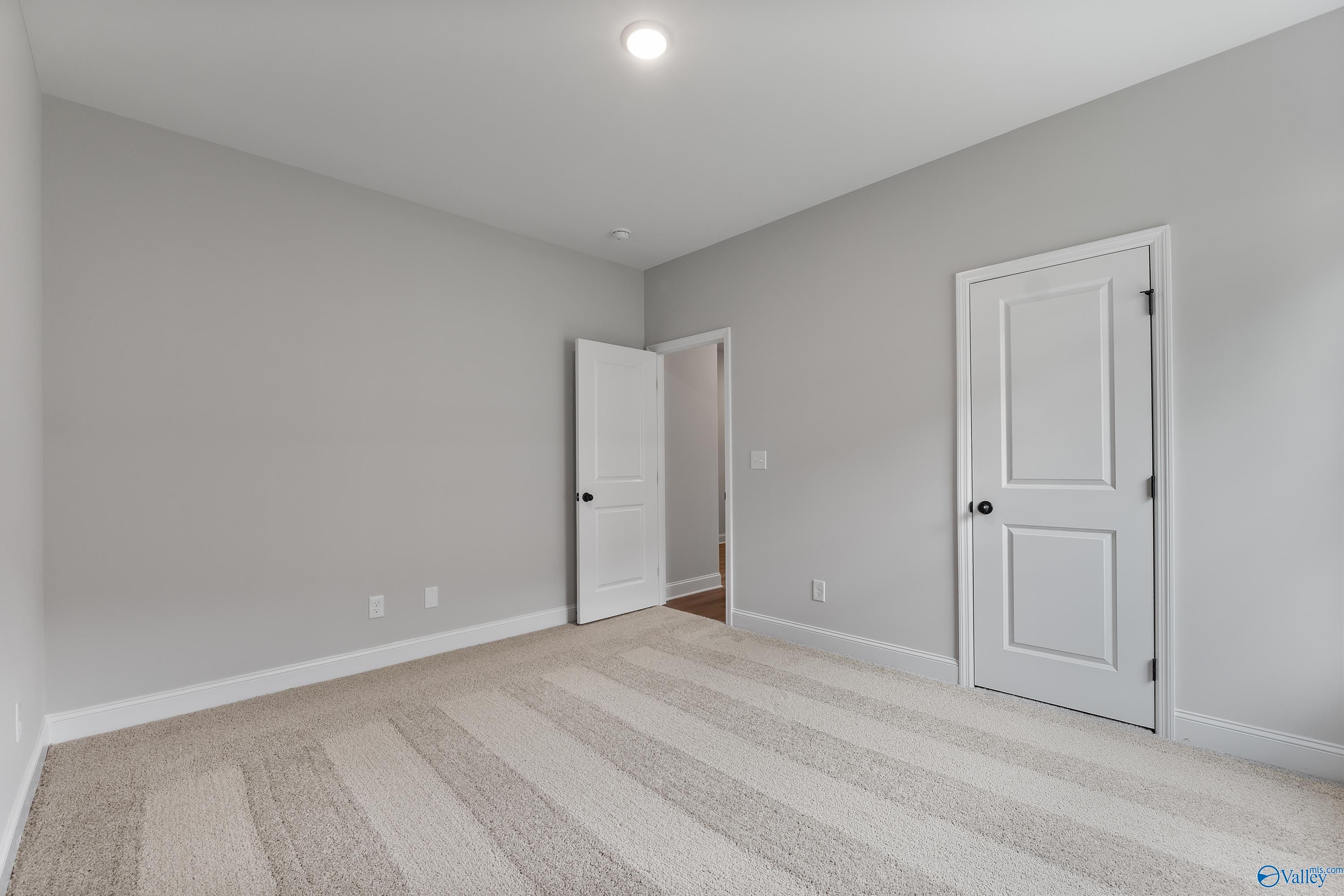 Spacious empty bedroom with light gray walls, striped beige carpet, white doors, and recessed lighting in Davidson Homes The Daphne, Huntsville AL