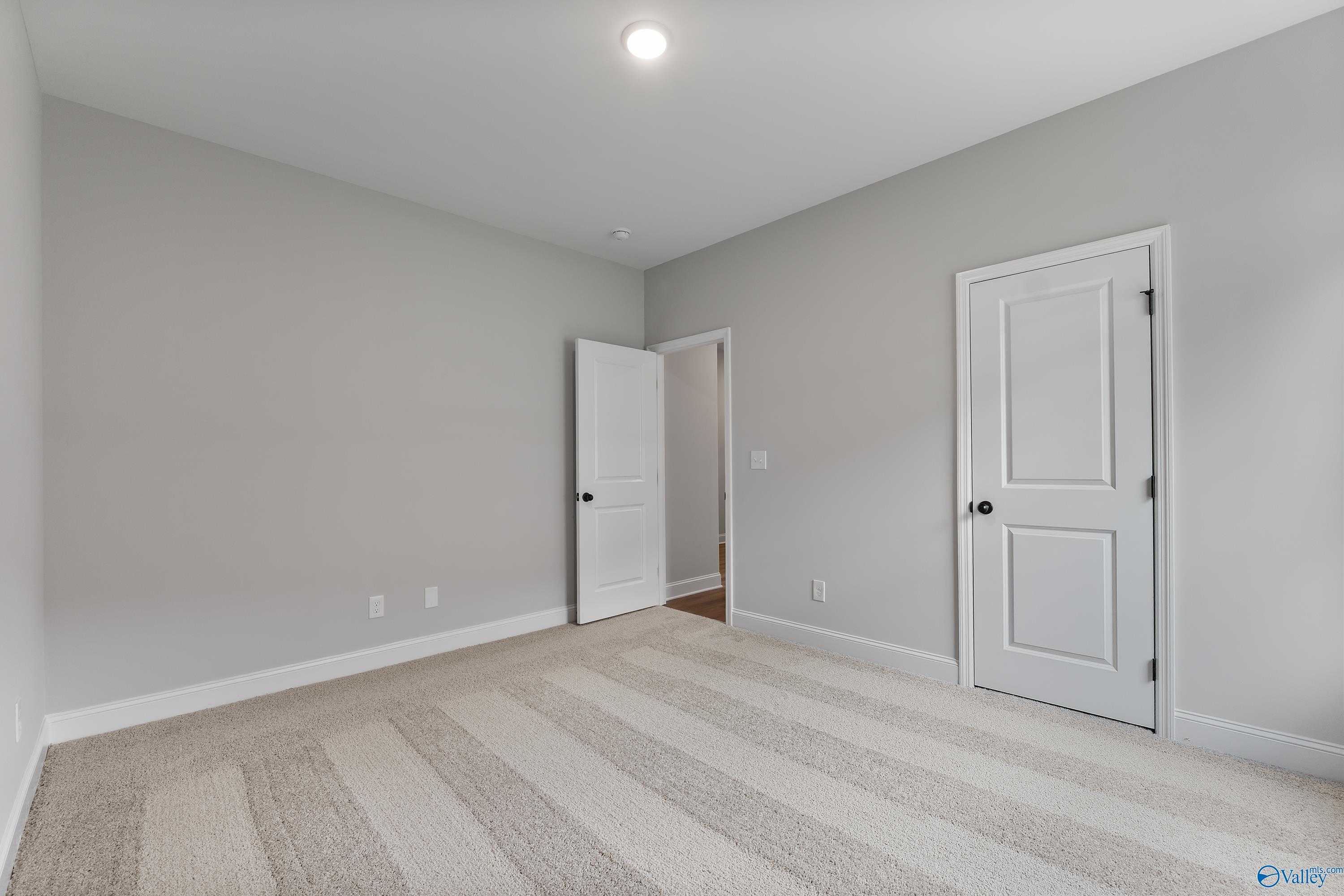 Spacious empty bedroom with light gray walls, striped beige carpet, white doors, and recessed lighting in Davidson Homes The Daphne, Huntsville AL