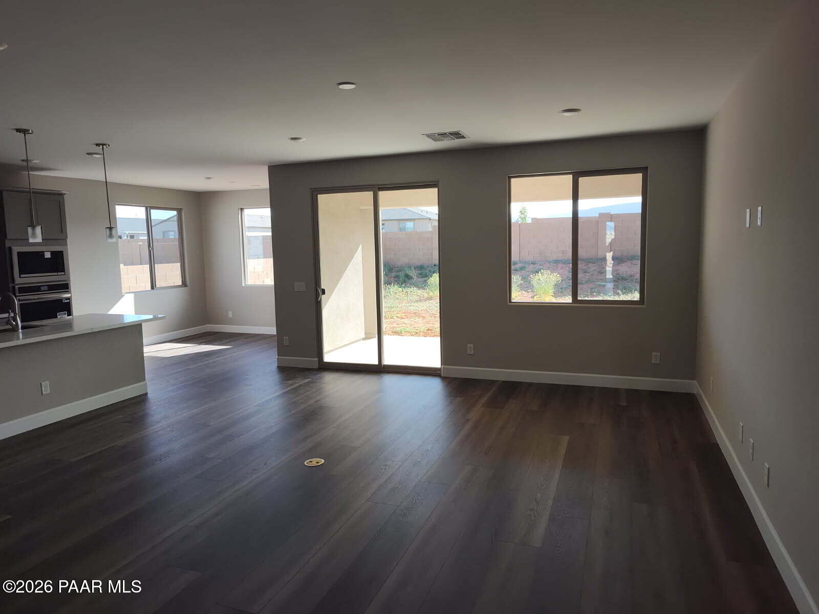 Open living area with kitchen island, stainless appliances, wood flooring, and sliding doors to desert backyard in The Harmony C, Prescott Valley, AZ