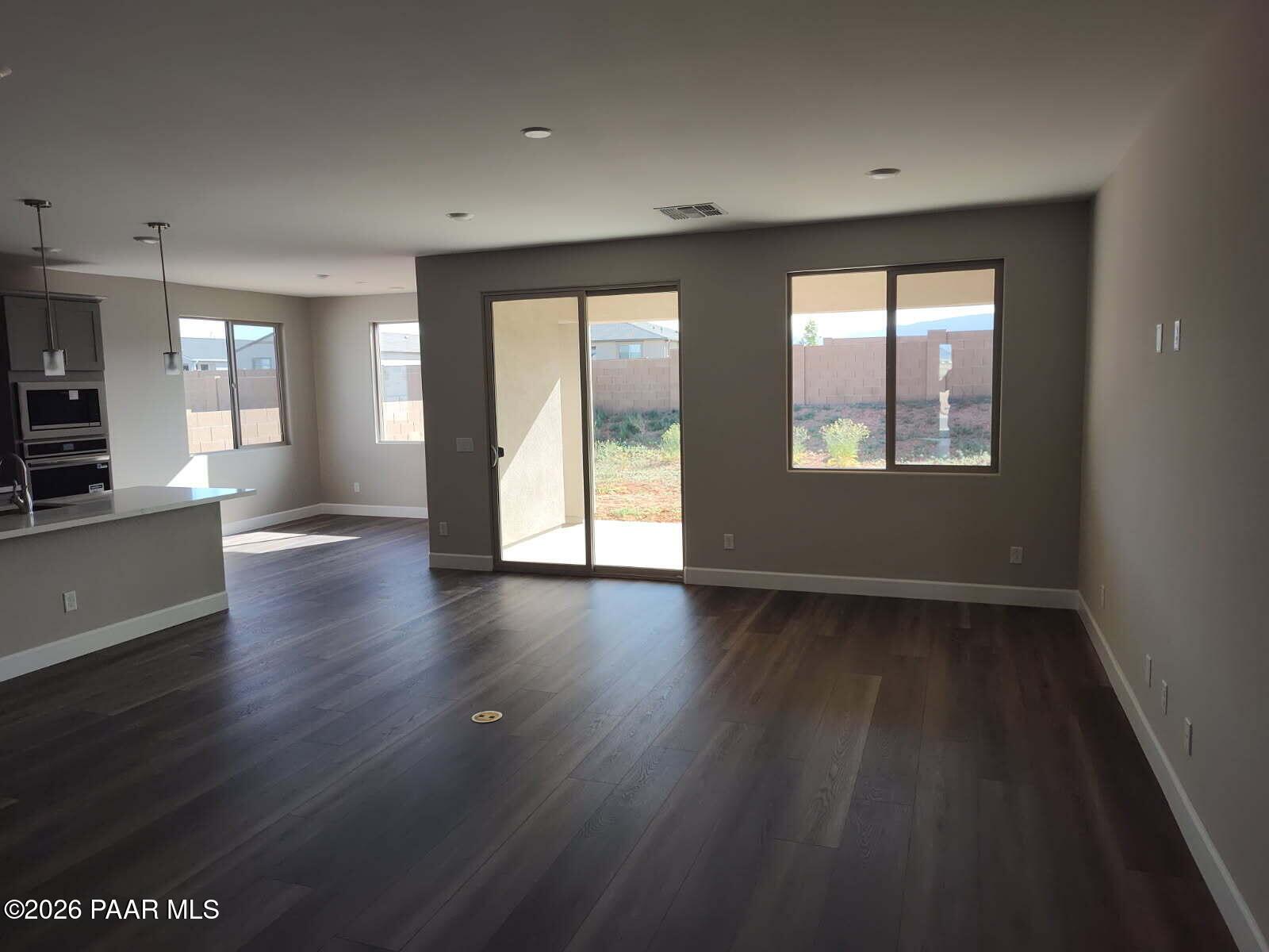 Open living area with kitchen island, stainless appliances, wood flooring, and sliding doors to desert backyard in The Harmony C, Prescott Valley, AZ
