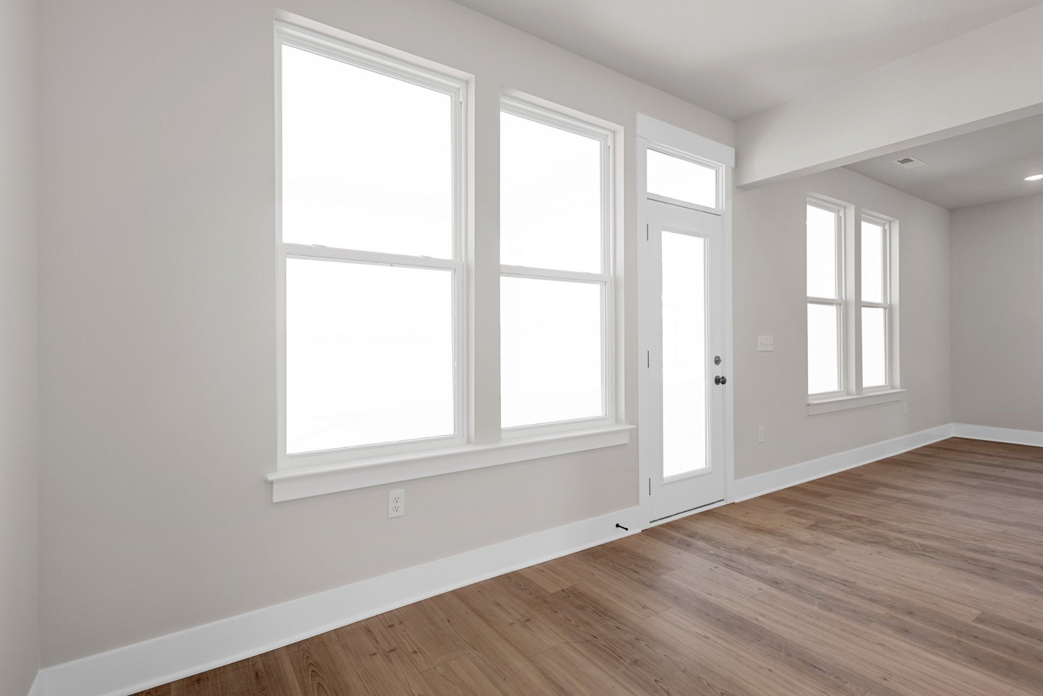 Bright sunlit room with large windows, gray walls, glass door, and hardwood floors in Davidson Homes The Willow B, Calista Farms