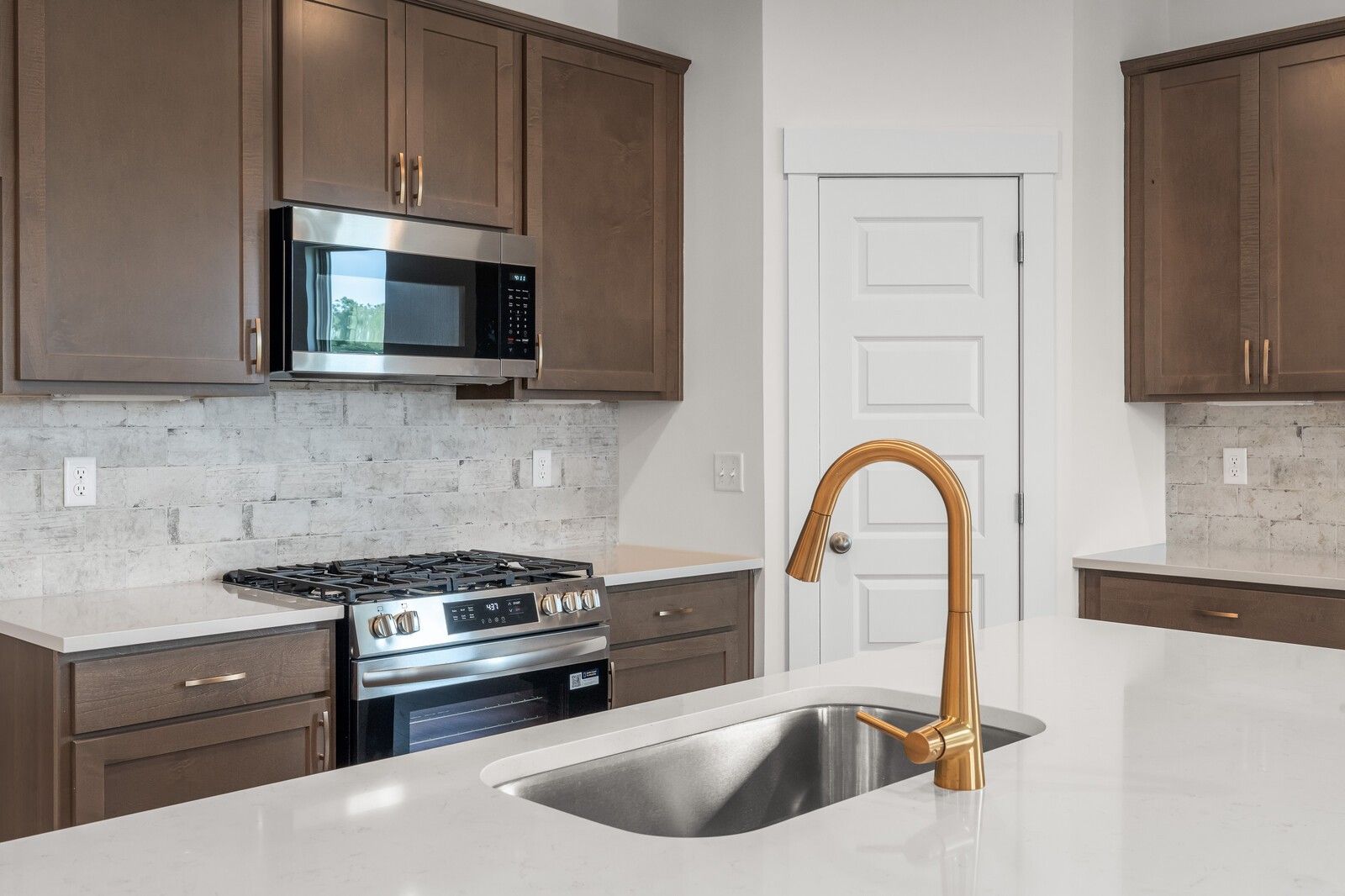 Modern kitchen with gold faucet, quartz countertops, and stainless steel appliances in The Prairie C at Woods Crossing.