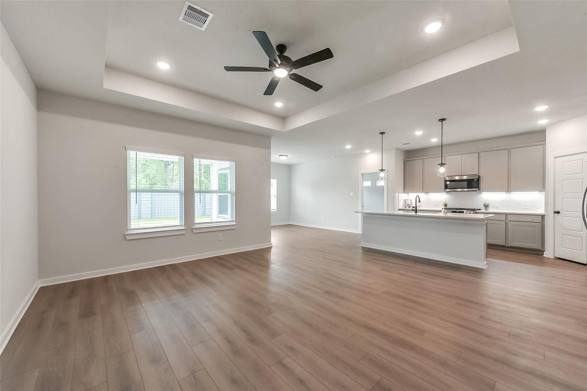 Open-concept living kitchen with hardwood floors, white island, stainless appliances in The Everett C, Sundance Cove, Crosby, Texas
