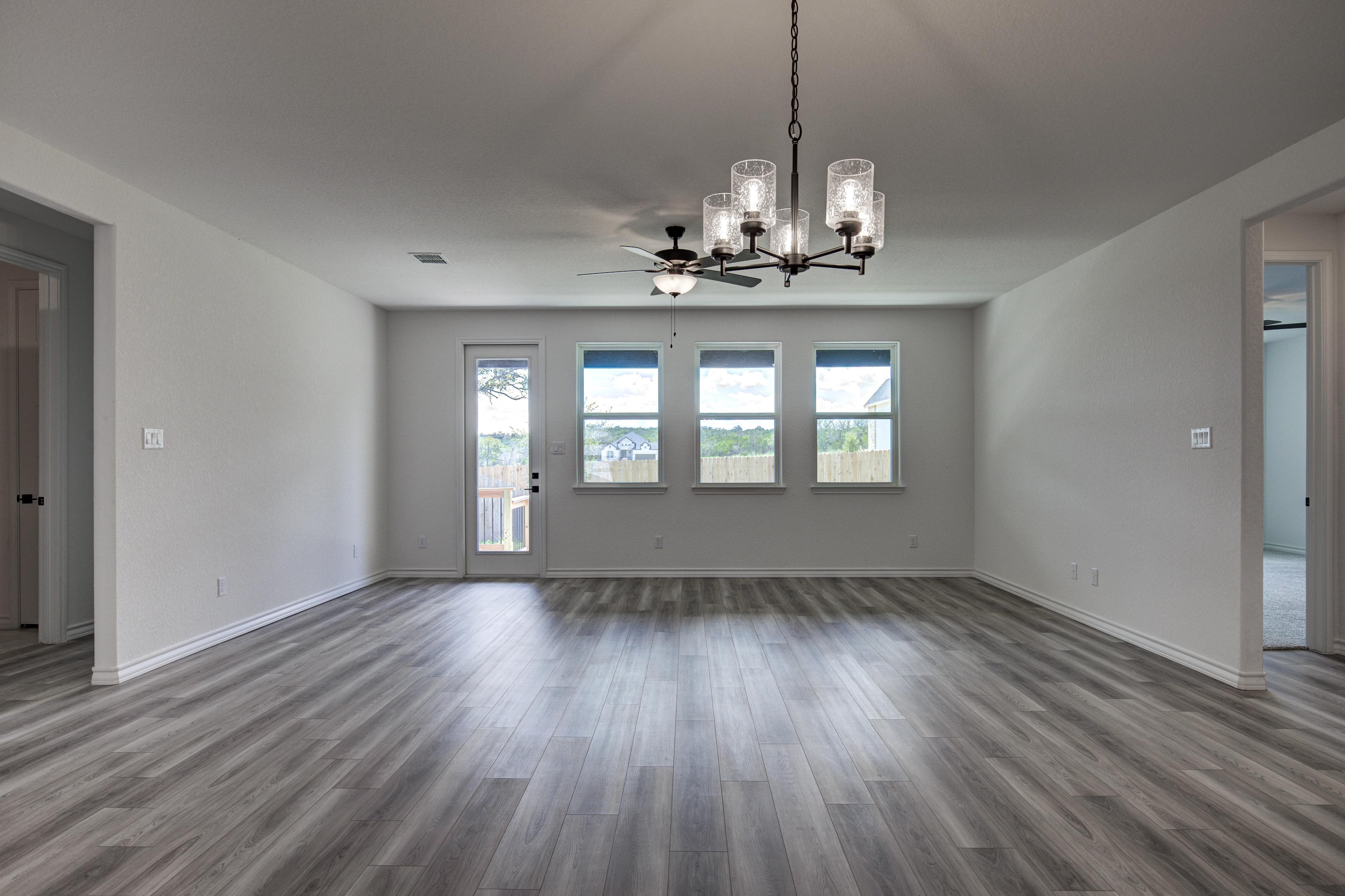 Spacious open-concept living room in The Lanier floor plan with vaulted ceiling, chandelier, ceiling fan, large windows, French doors, and hardwood floors