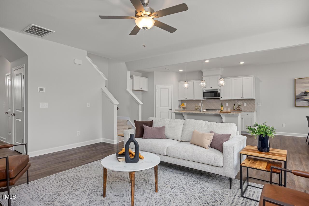 Open-concept living room with white sofa, ceiling fan, hardwood floors, and kitchen island in The Grace A by Davidson Homes, Zebulon, NC