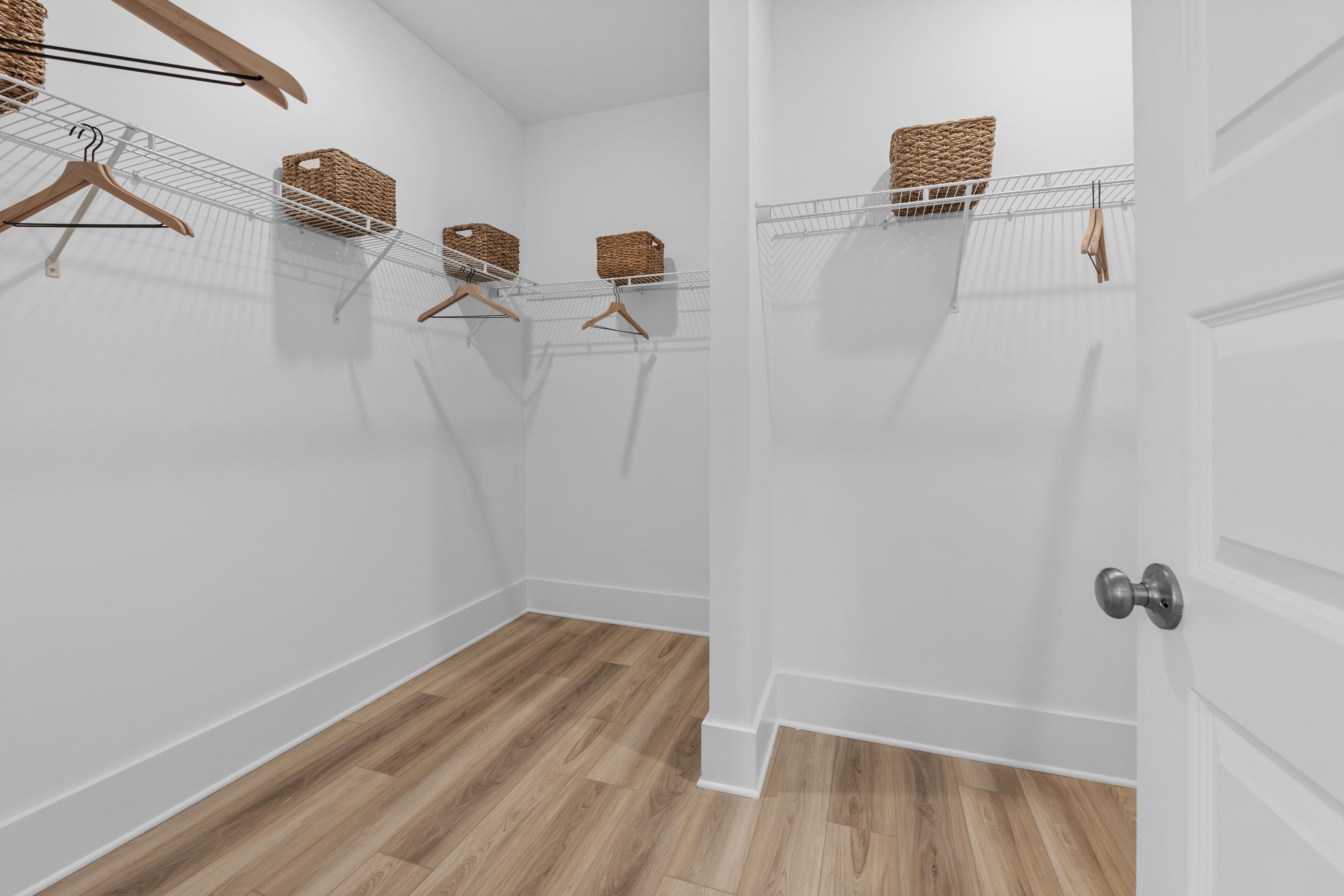 Spacious walk-in closet at The Highlands in Arab, Alabama with white walls, wooden hangers and wicker baskets