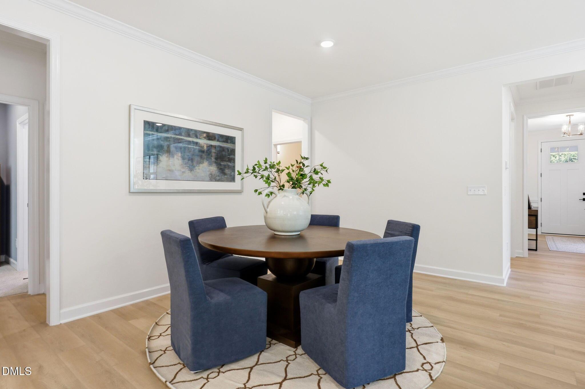 Modern dining area with round wood table, blue upholstered chairs, and decor in The Aspen B home at Wendell Ridge, NC.