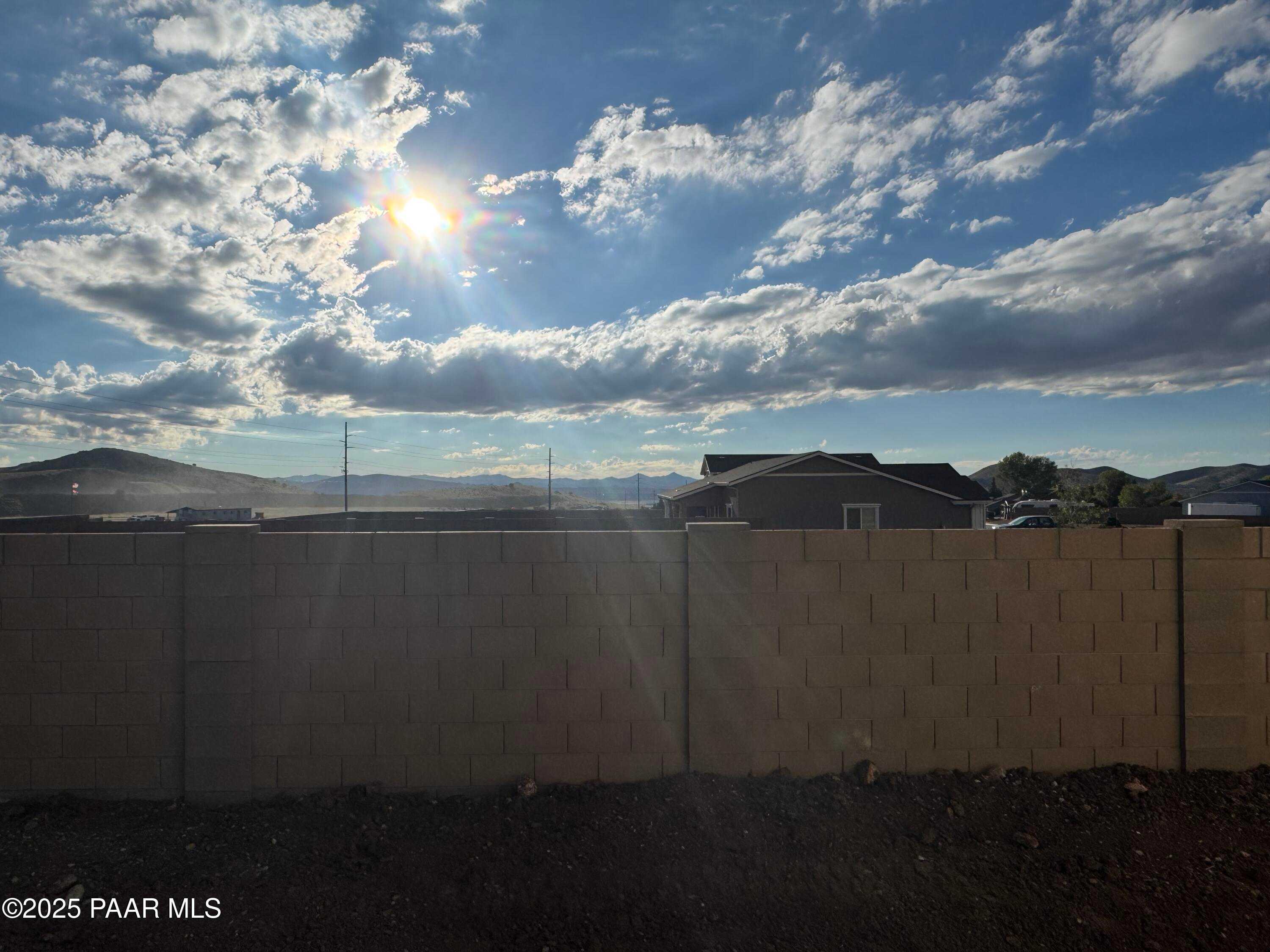 Sunny backyard with beige block wall, distant mountain views, and neighborhood homes in Evermore Homes The Sunrise A, Prescott Valley, Arizona