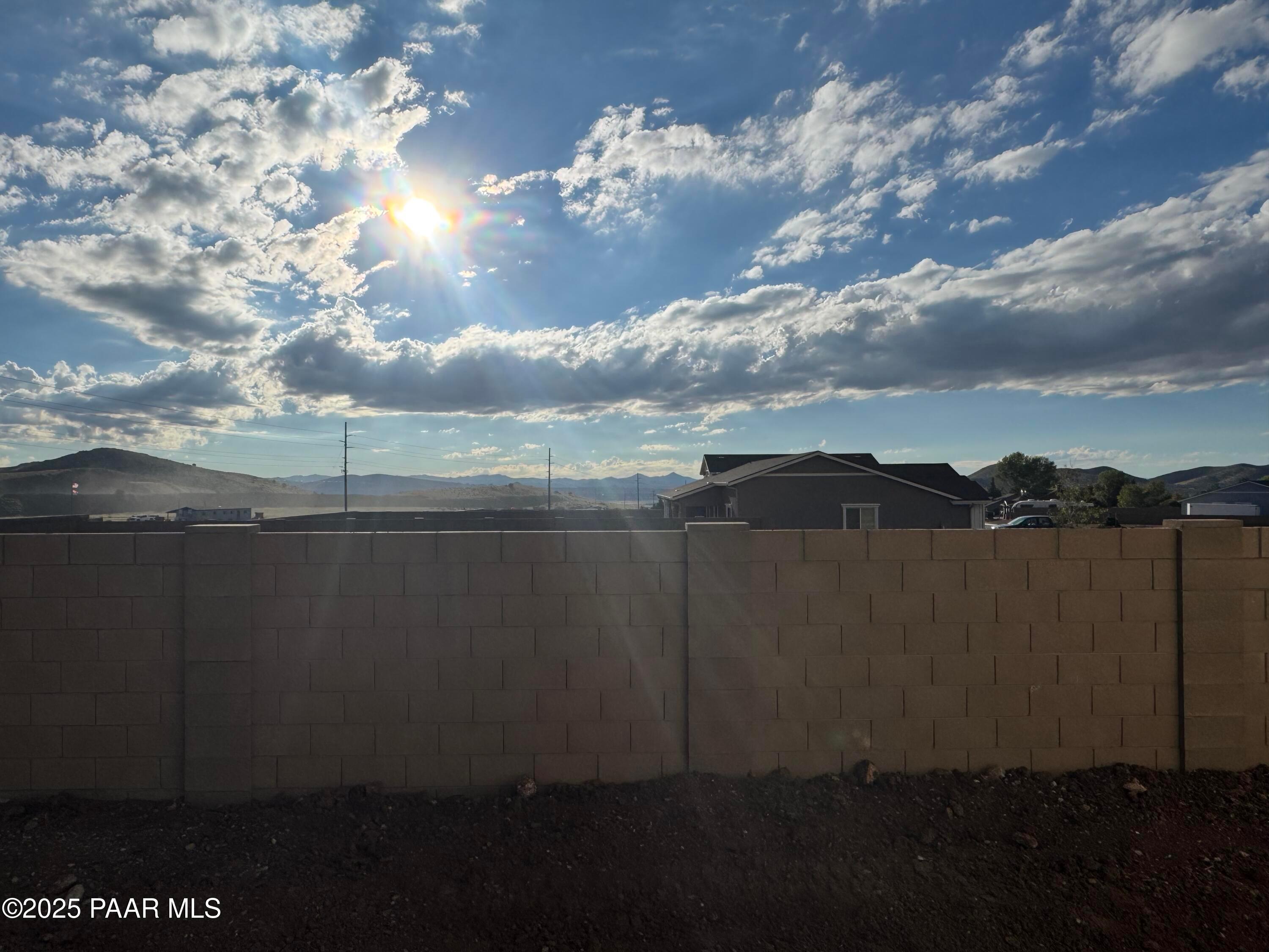 Sunny backyard with beige block wall, distant mountain views, and neighborhood homes in Evermore Homes The Sunrise A, Prescott Valley, Arizona