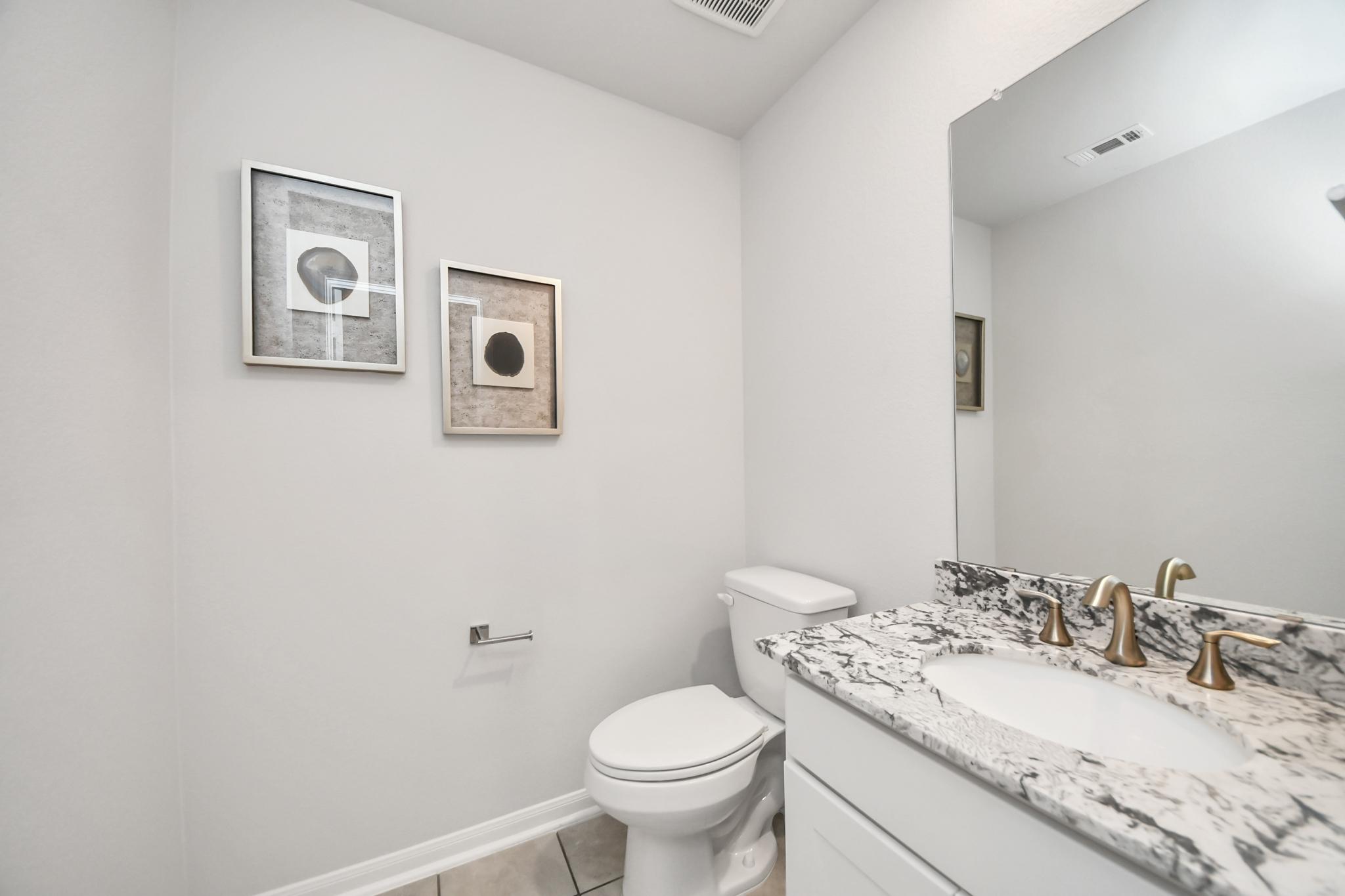Modern powder room at Sunterra in Katy, TX by Davidson Homes featuring granite countertops and gold faucet fixtures.