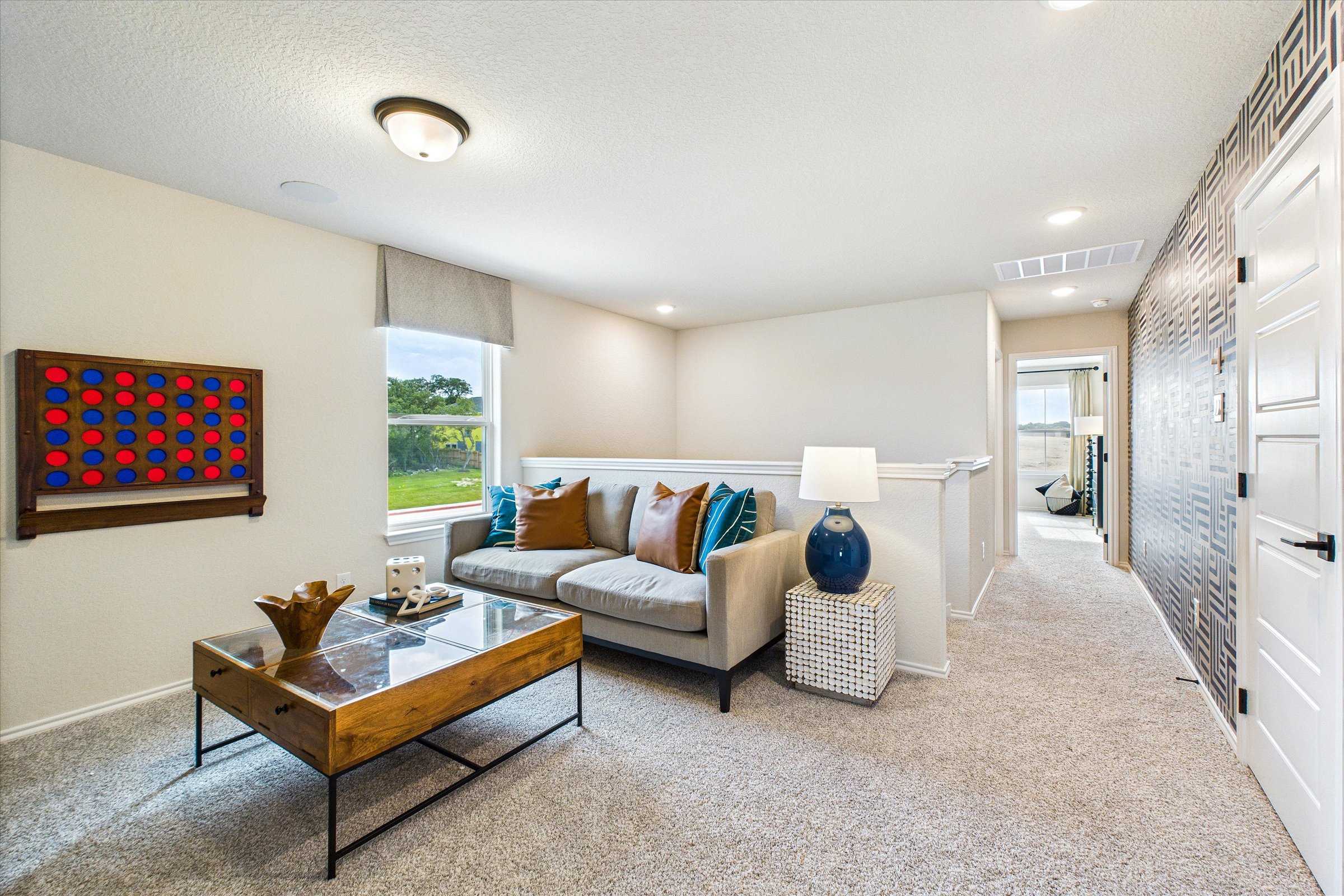 Cozy loft living area at Meadows at Oak Creek in San Antonio TX with gray sofa, wooden coffee table, and window views