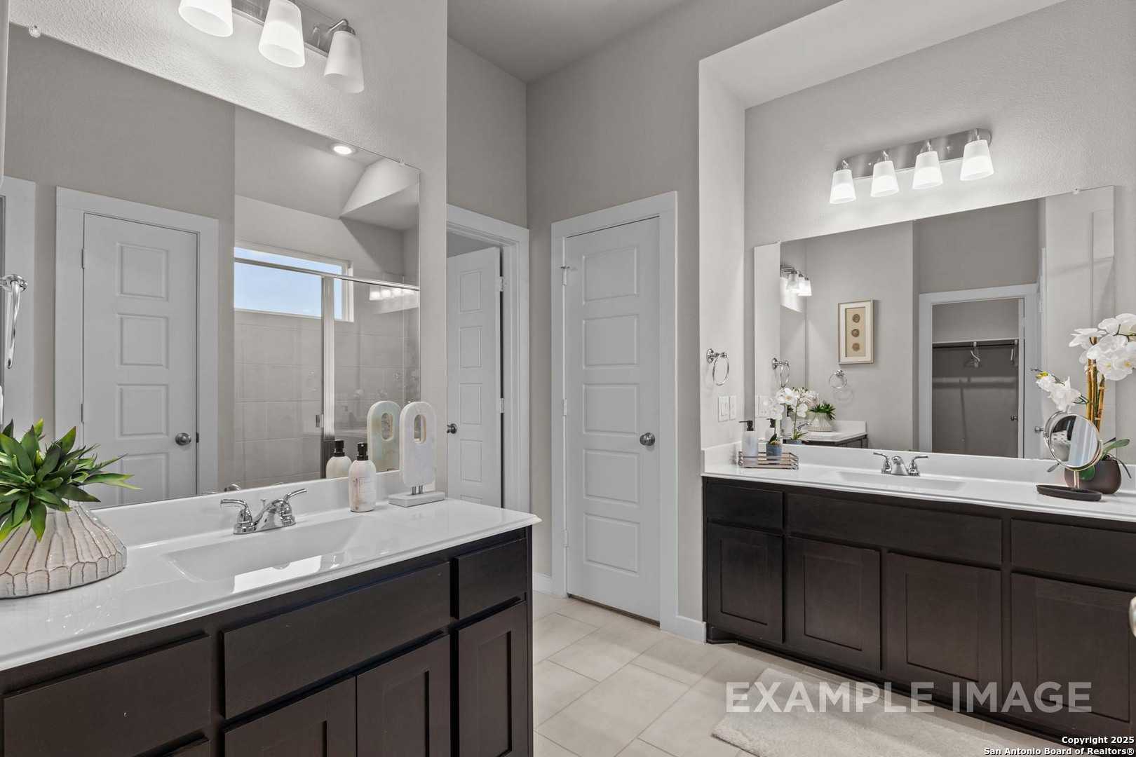 Elegant master bathroom featuring double vanity with dark cabinets, dual sinks, and mirrors in Davidson Homes The Collin B, Seguin, Texas