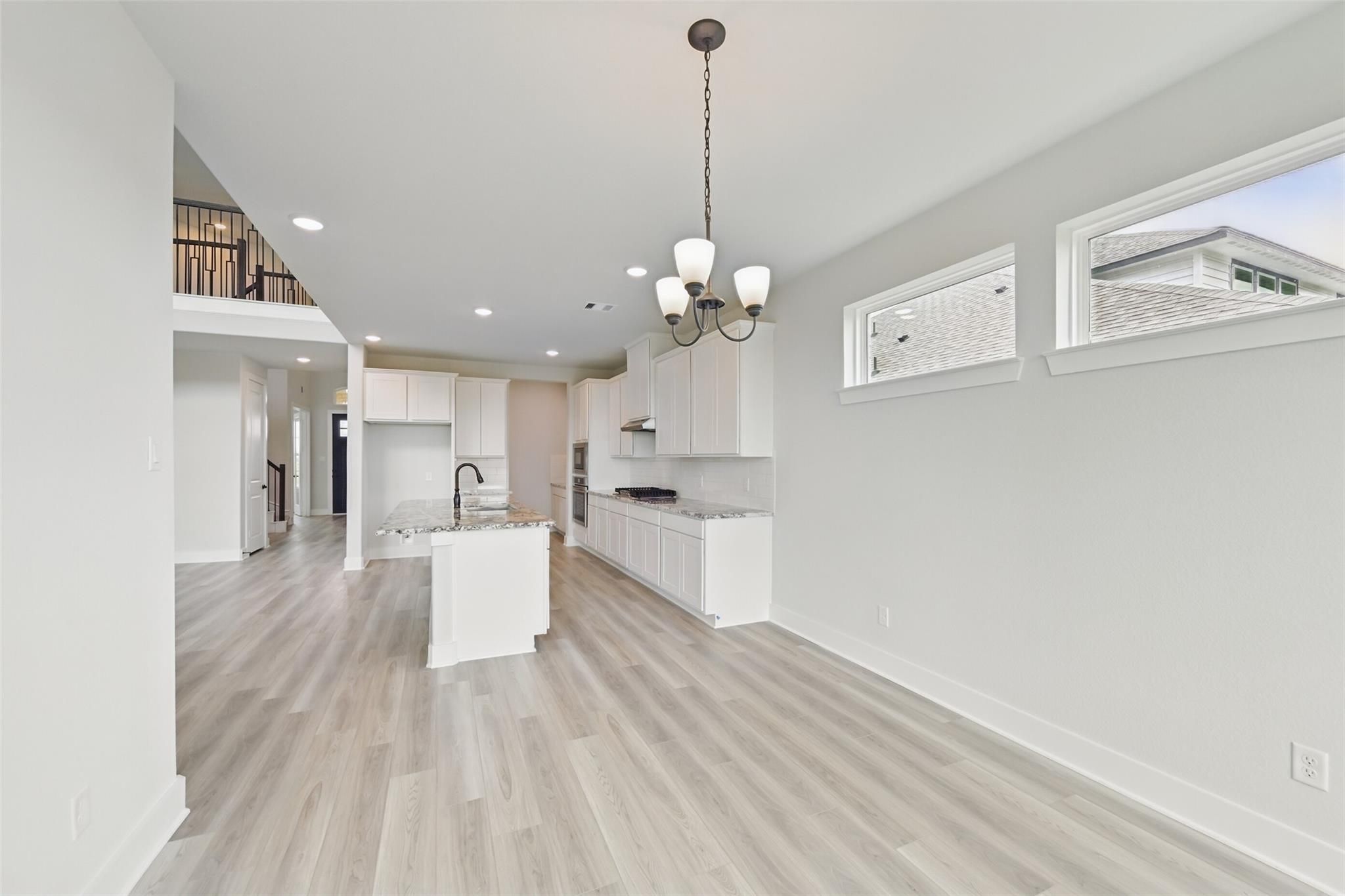 Spacious open kitchen with white cabinets, large island, stainless appliances, and hardwood floors in Davidson Homes The Victoria C, Lago Mar, Texas City