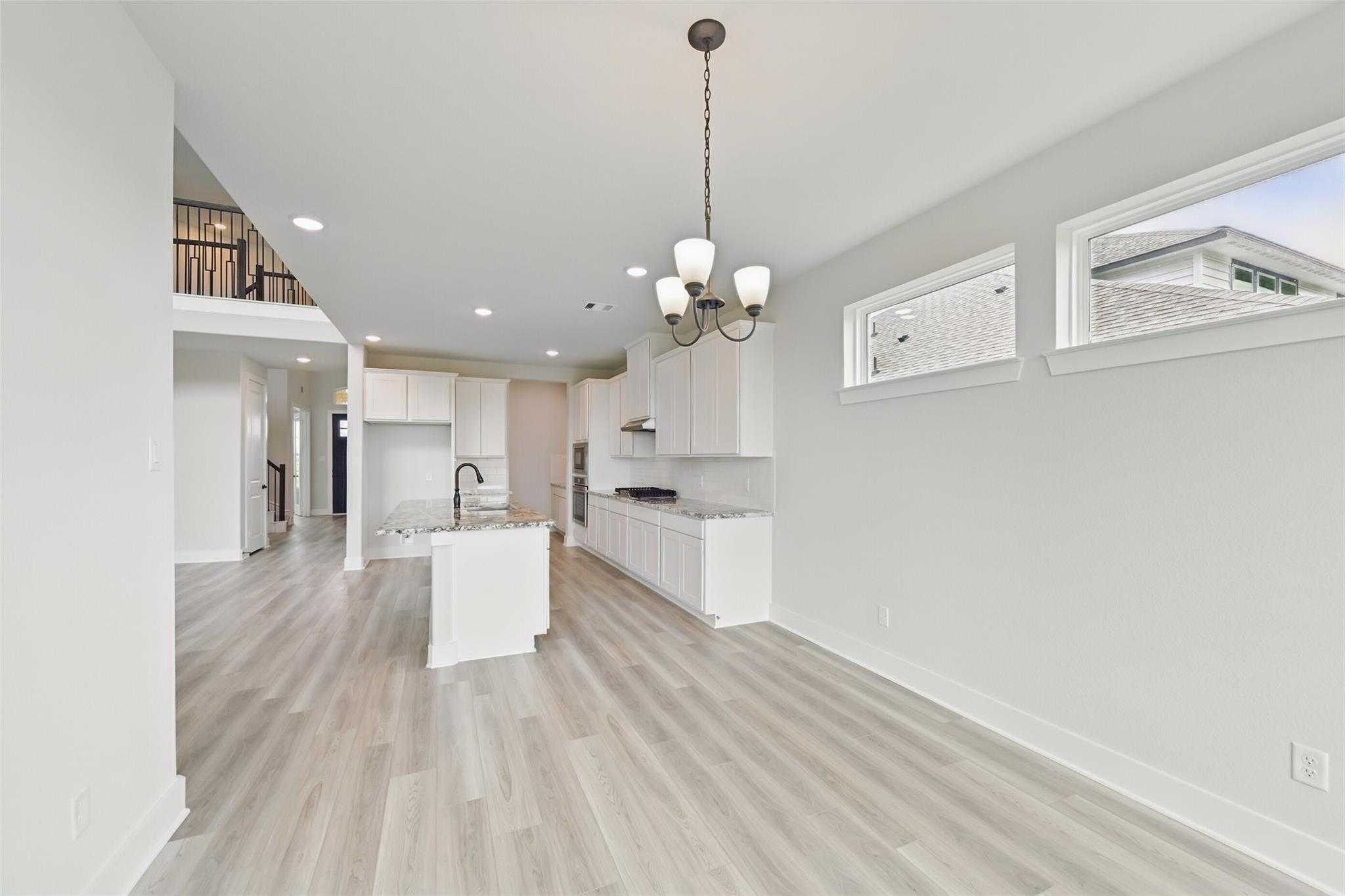 Modern open-concept kitchen with white cabinets, center island, and hardwood floors in Davidson Homes The Victoria C, Lago Mar, Texas City