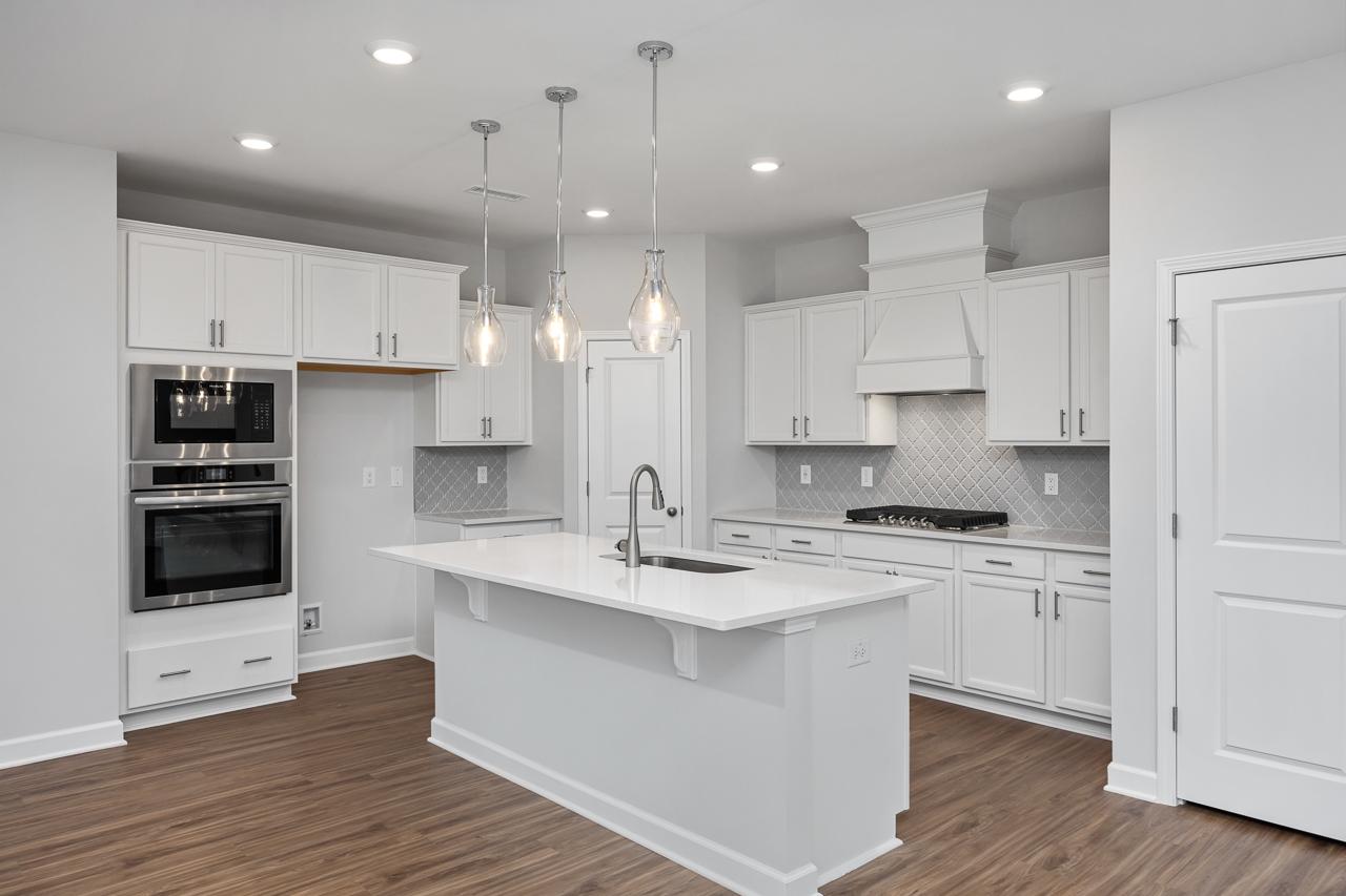 Spacious white kitchen in The Durham C with shaker cabinets, large island sink, gas cooktop, double ovens, and pendant lights