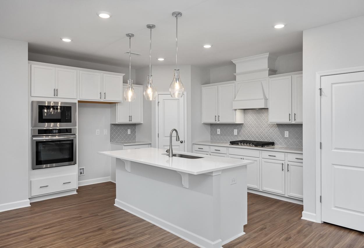 Spacious white kitchen in The Durham C with shaker cabinets, large island sink, gas cooktop, double ovens, and pendant lights
